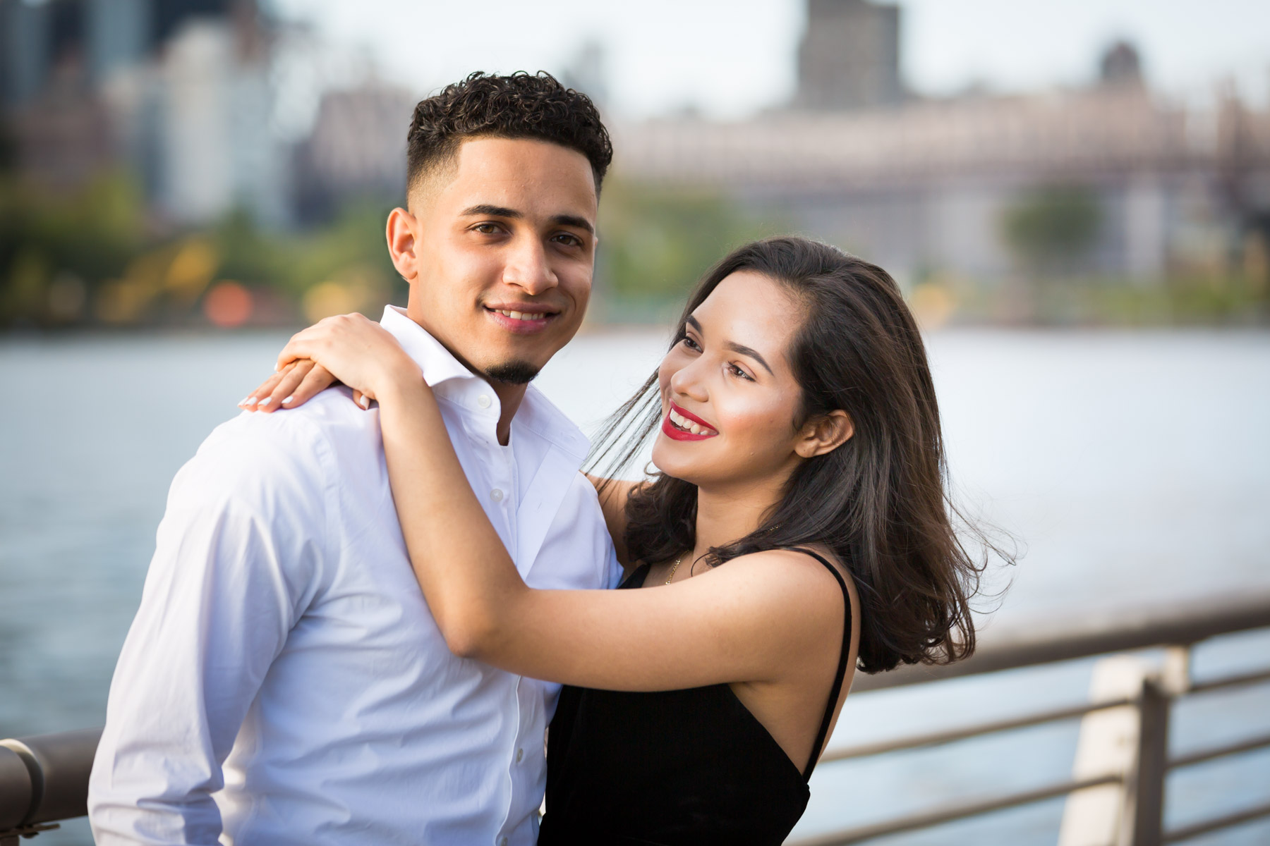 Couple hugging in front of railing with city skyline in background for an article on how to beat the summer heat during a photo shoot