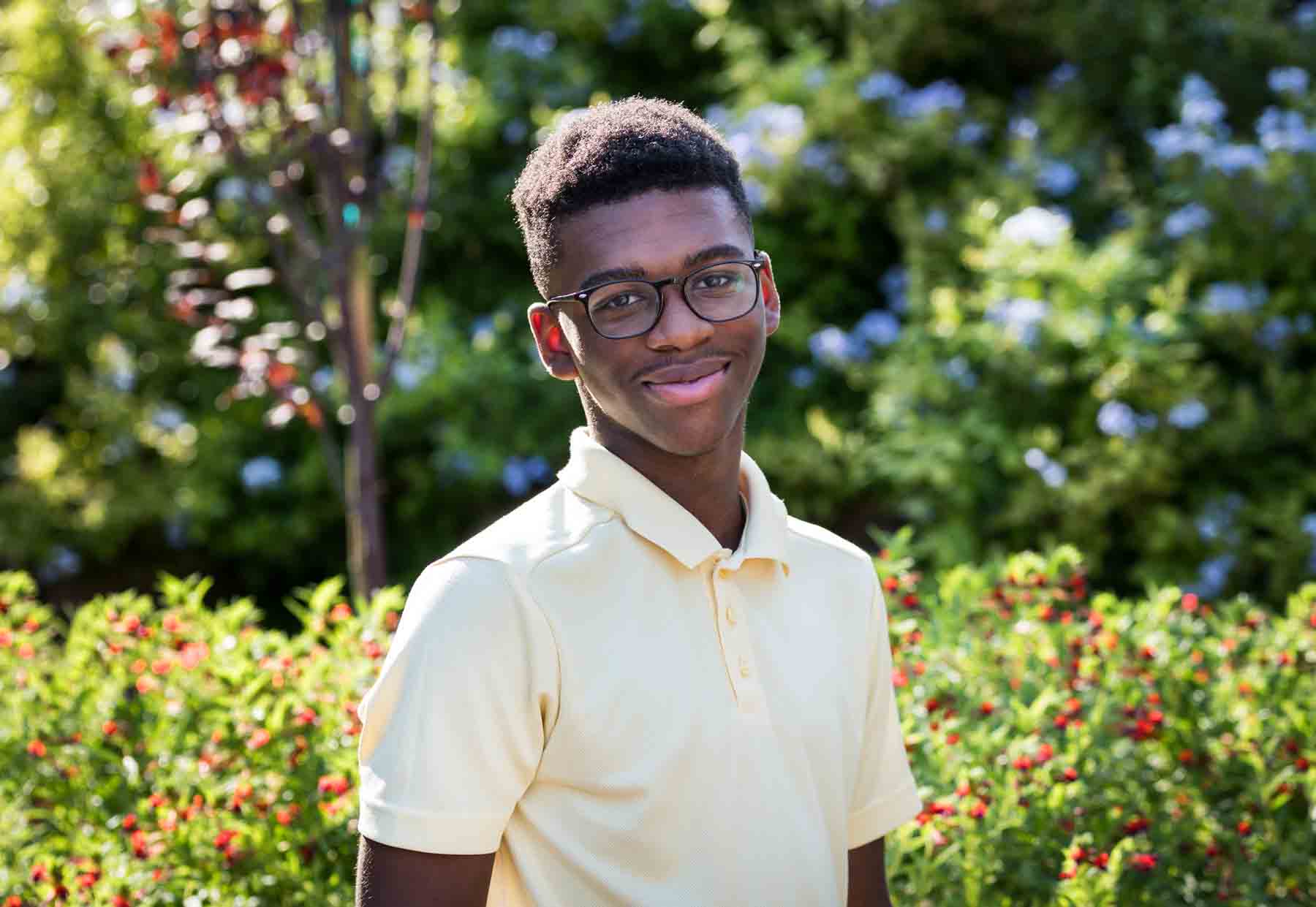 Young African American man wearing yellow shirt and glasses standing in front of plants in the Japanese Tea Garden