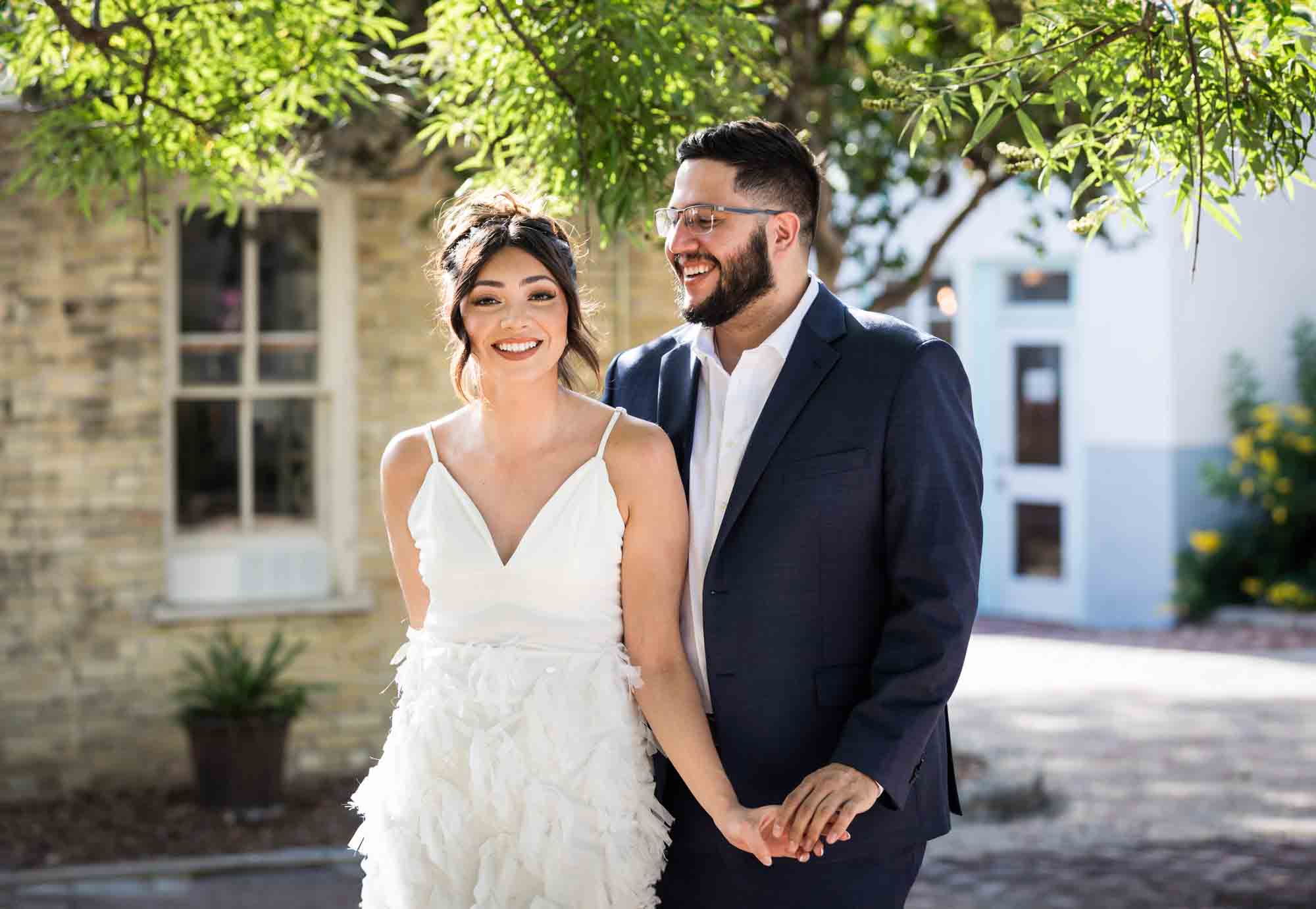 La Villita engagement photos of couple holding hands in patio with tree branch in background