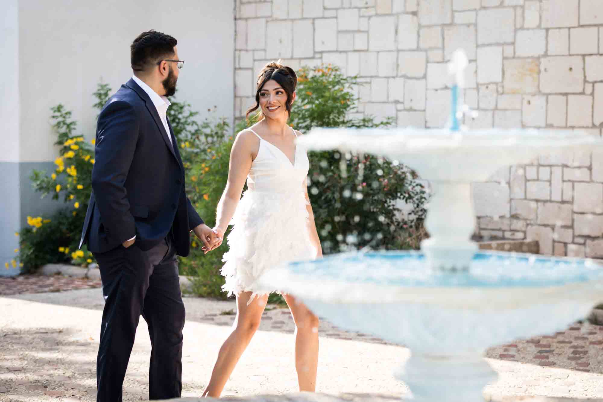 La Villita engagement photos of couple holding hands and walking around fountain