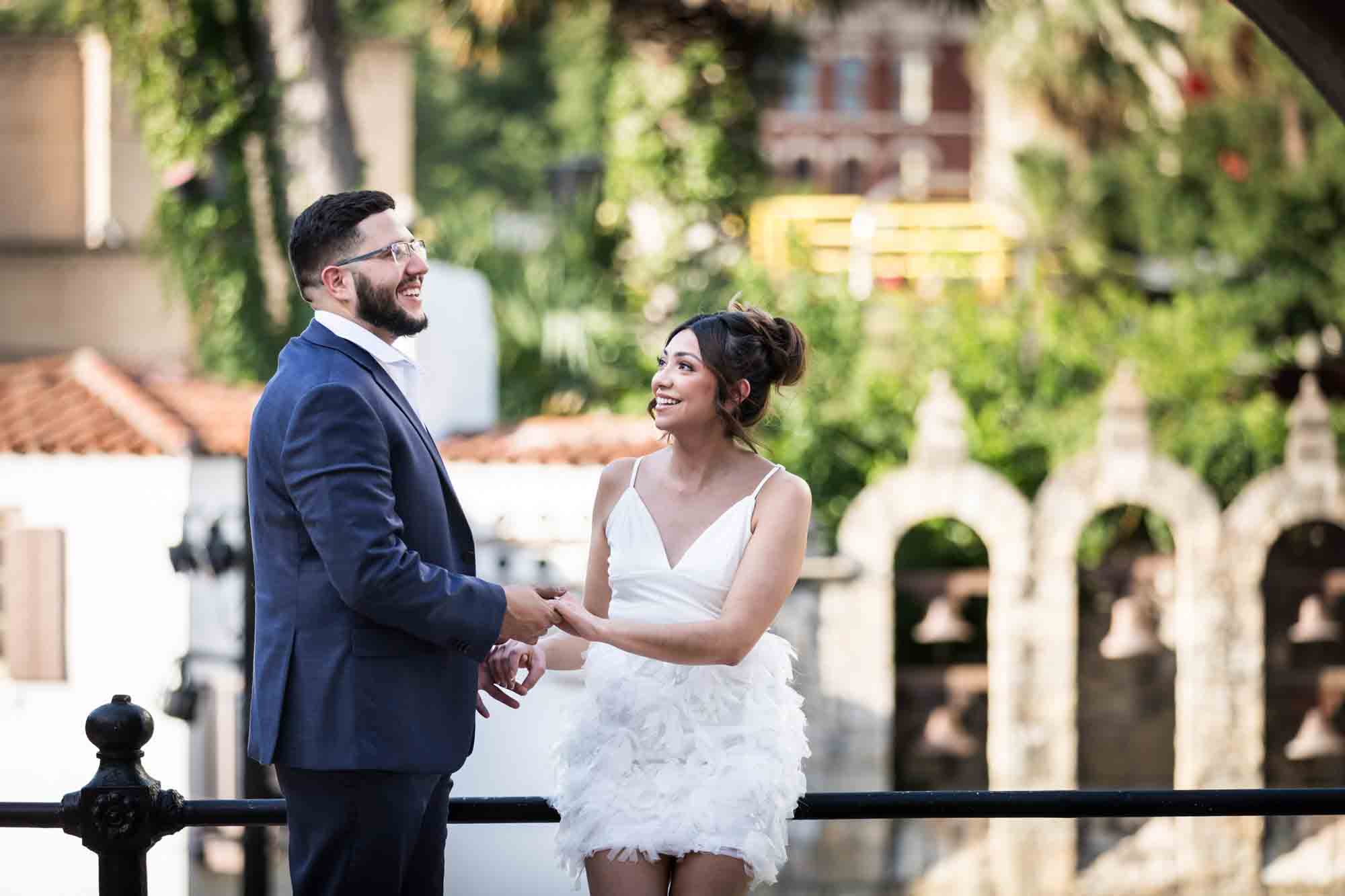 La Villita engagement photos of couple holding hands and against railing with Arneson River Theatre in background