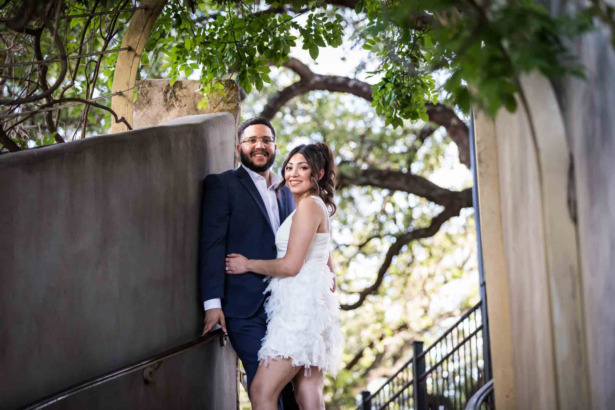 La Villita engagement photos of couple hugging at top of staircase with trees in background