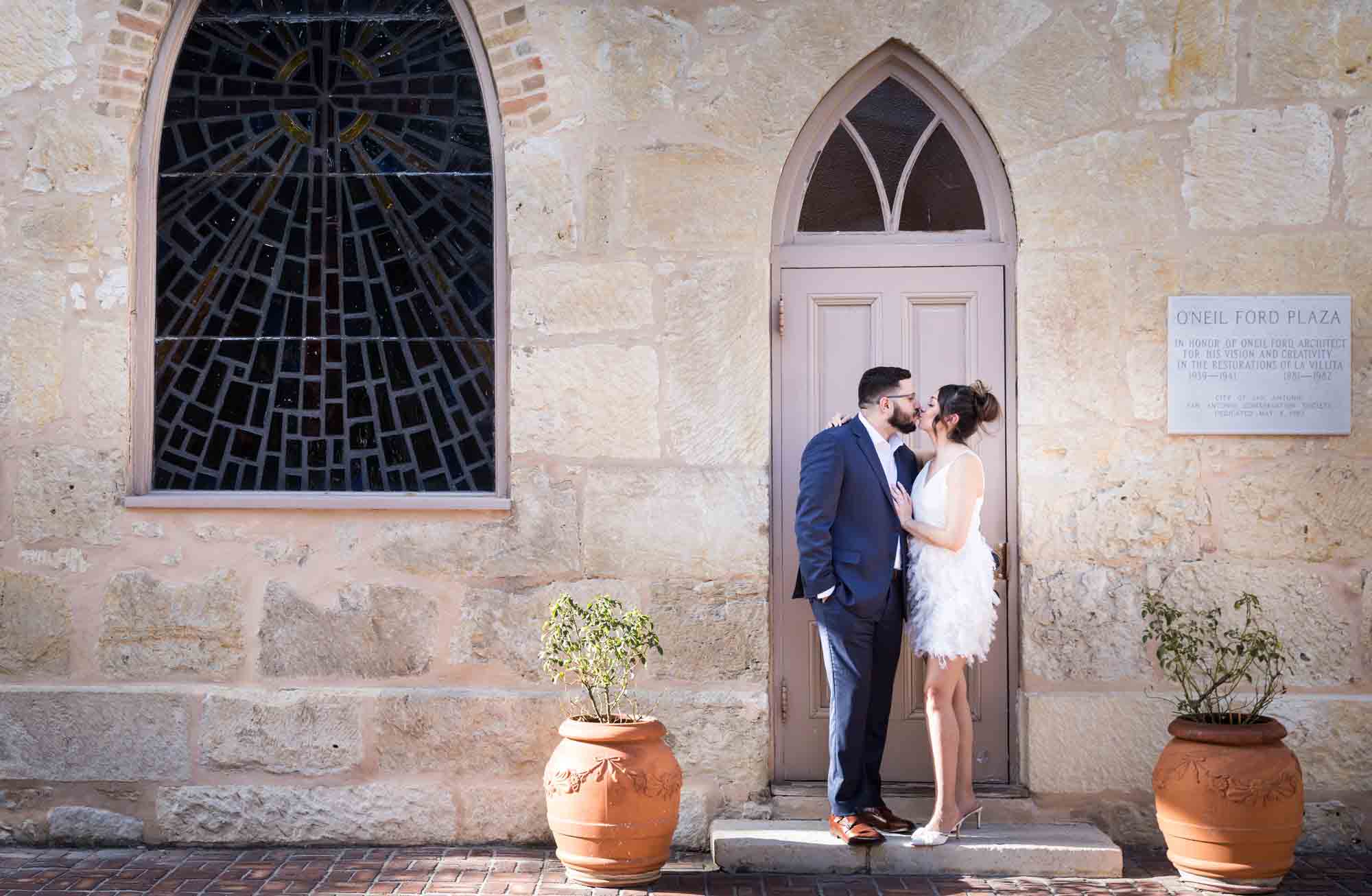 La Villita engagement photos of couple kissing against church door with stained glass window in corner