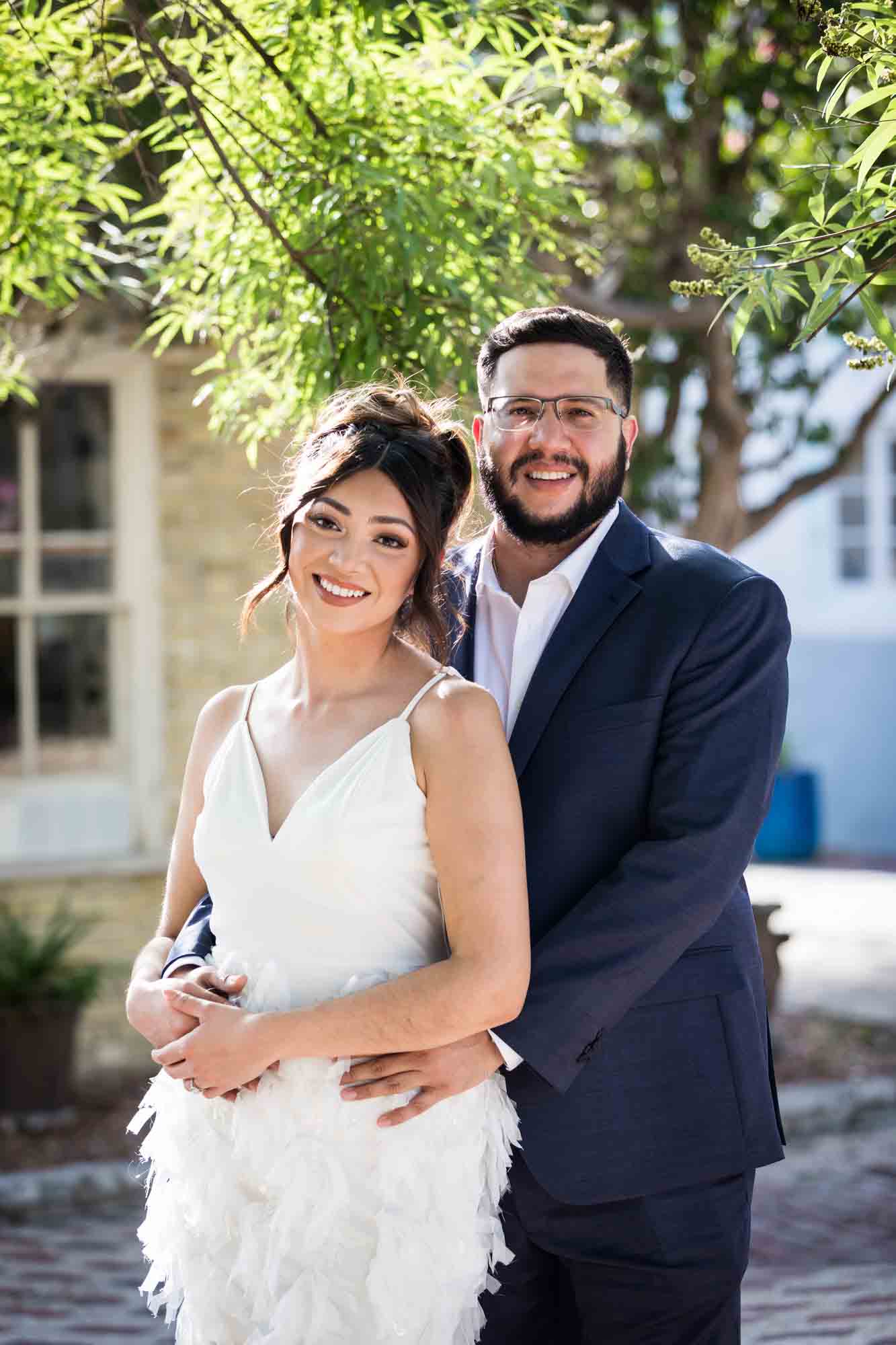 La Villita engagement photos of couple hugging in patio with tree branch in background