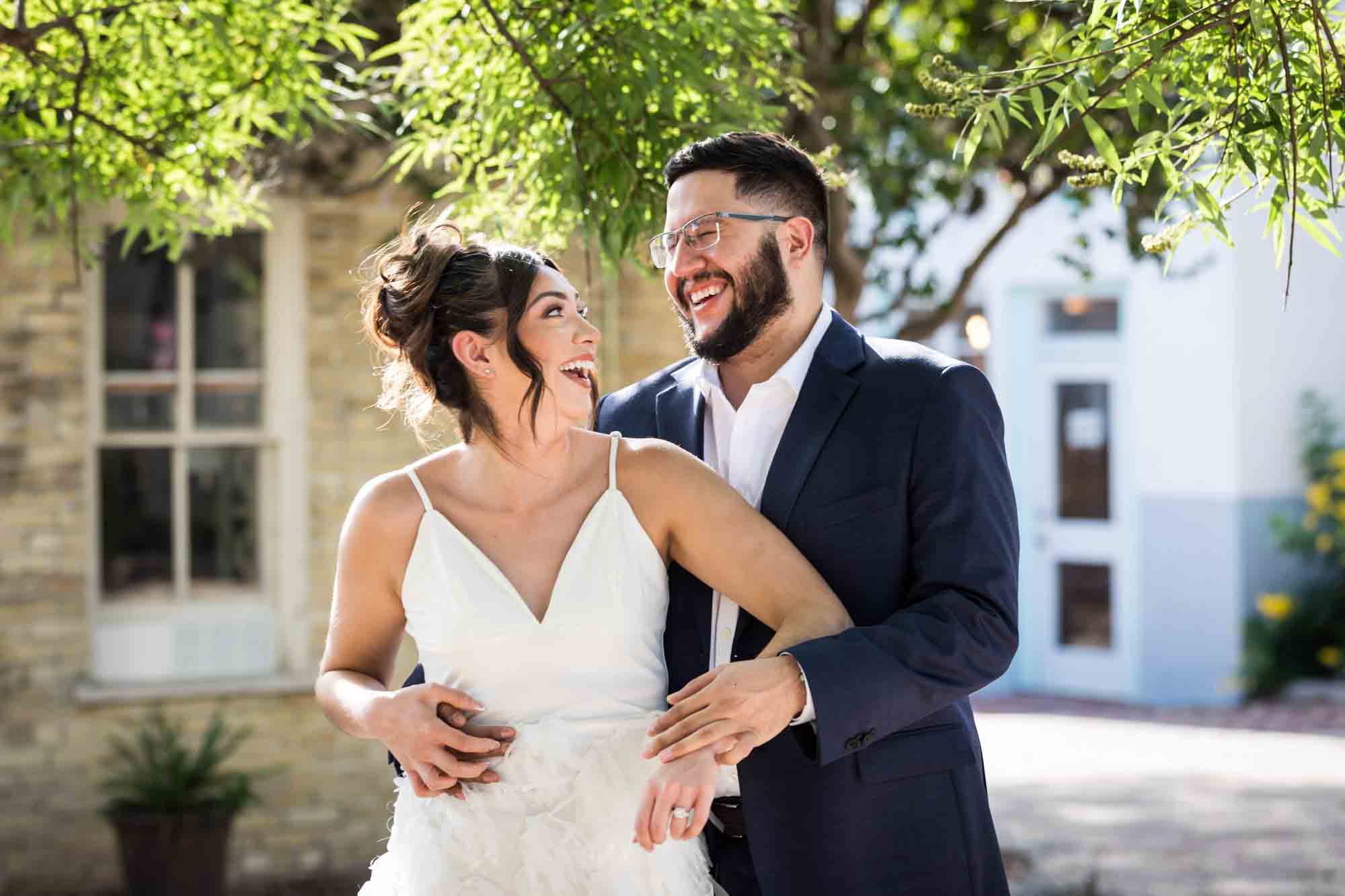 La Villita engagement photos of couple hugging in patio with tree branch in background