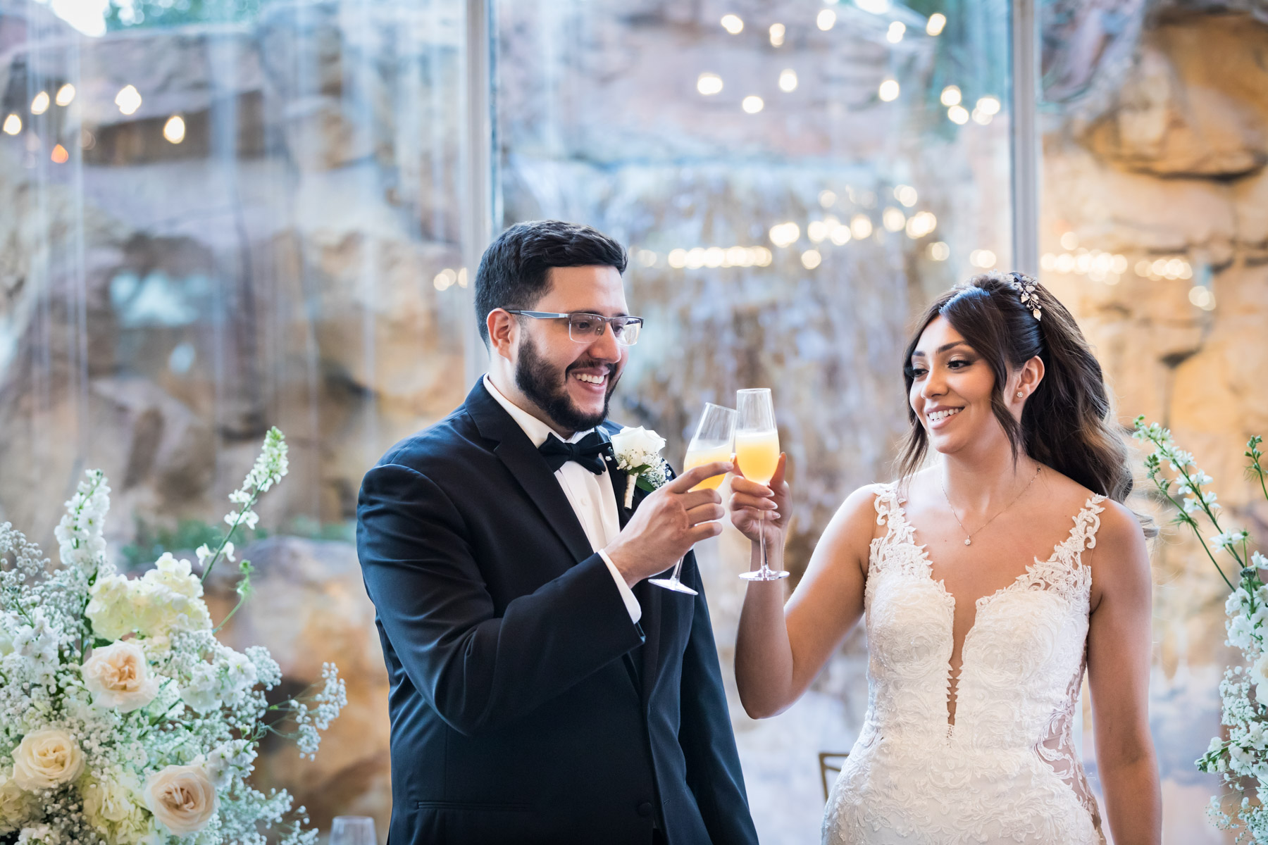 Bride and groom clinking champagne glasses in front of glass wall and white flowers at an Old San Francisco Steakhouse wedding