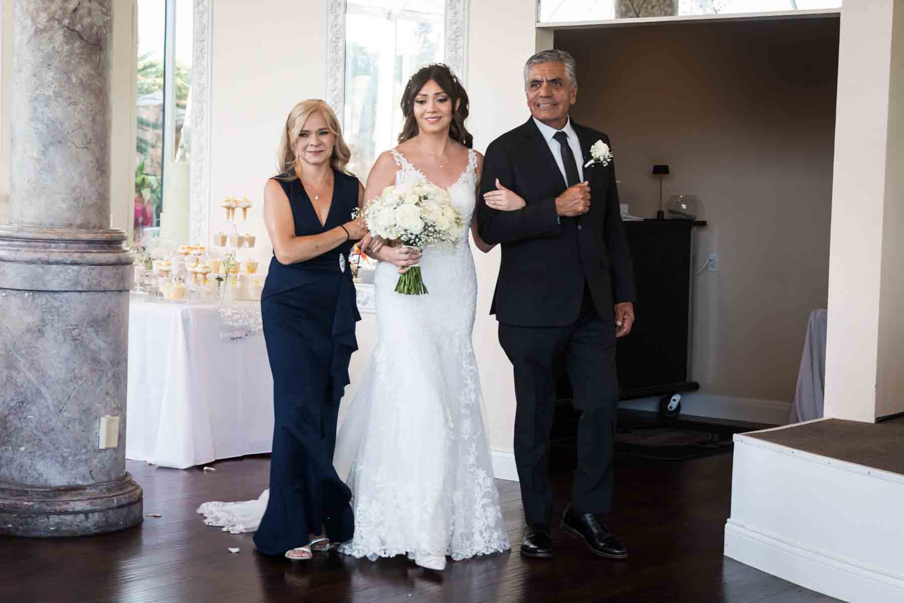 Bride escorted by parents walking down aisle during ceremony at an Old San Francisco Steakhouse wedding