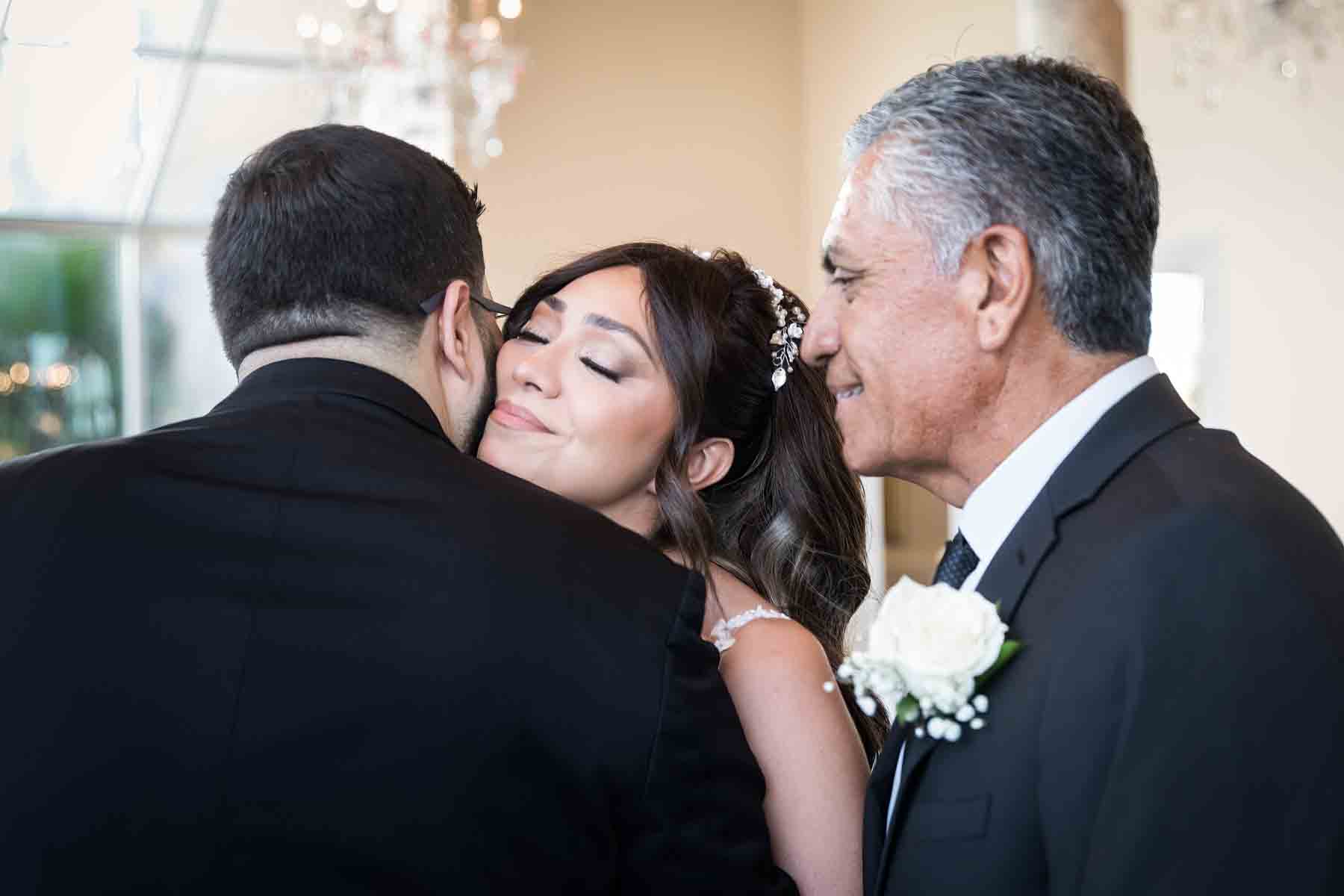 Groom kissing bride with eyes closed in front of father during ceremony at an Old San Francisco Steakhouse wedding