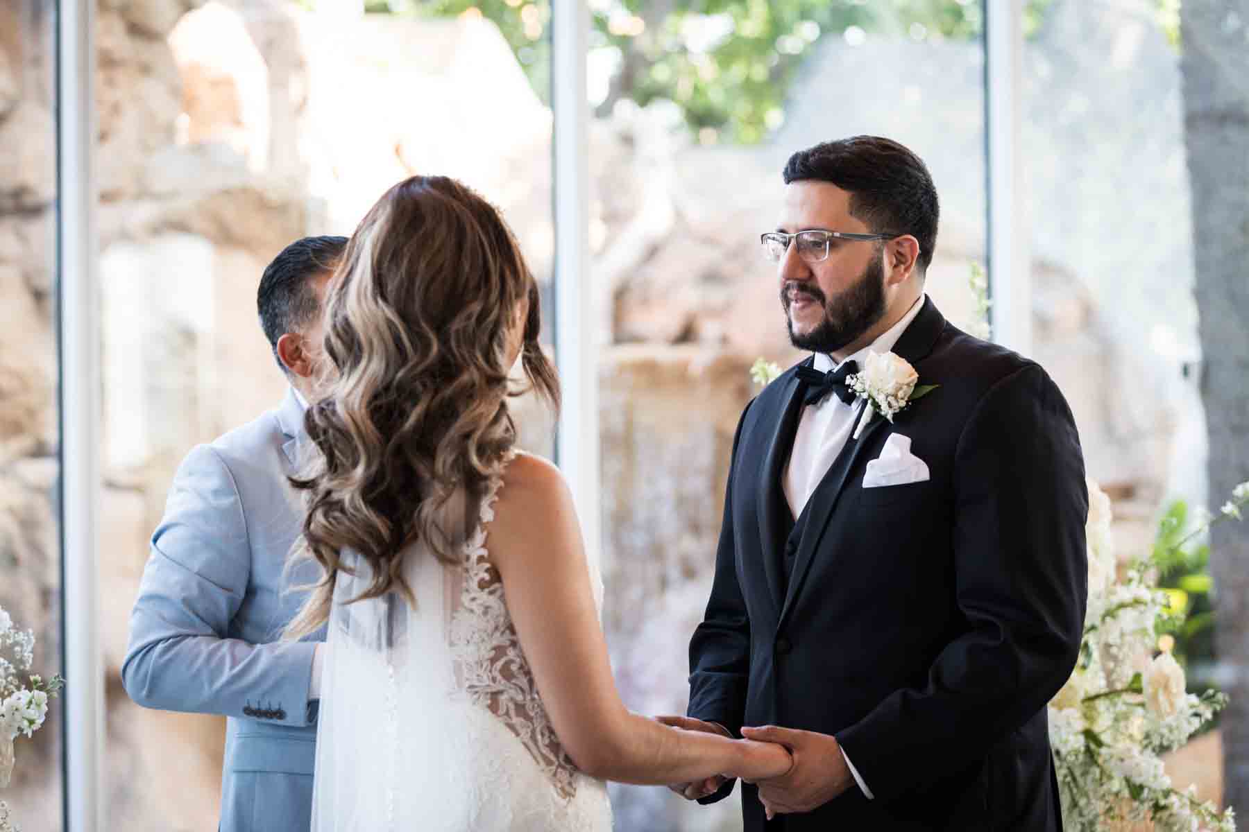 Bride and groom holding hands in front of officiant and glass wall at an Old San Francisco Steakhouse wedding