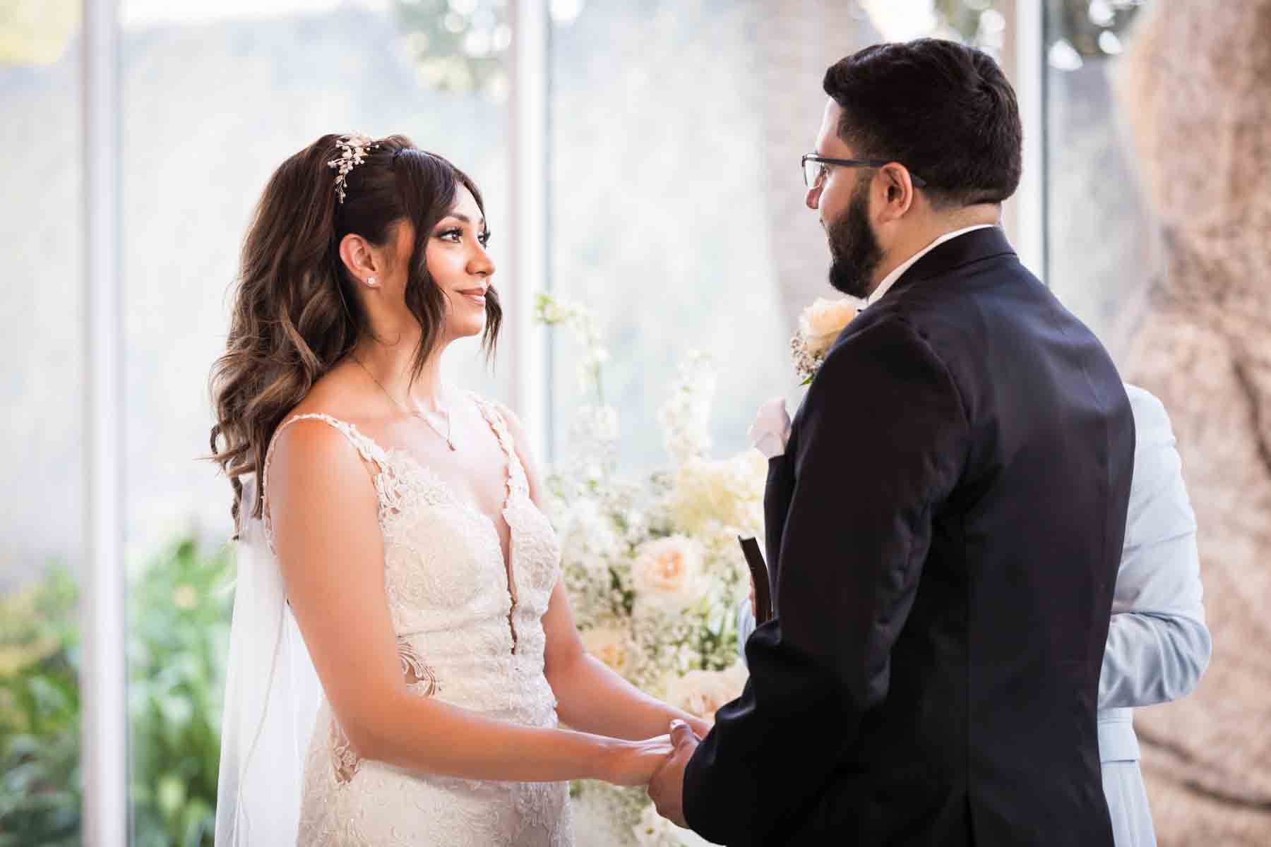 Bride and groom holding hands in front of officiant and glass wall at an Old San Francisco Steakhouse wedding