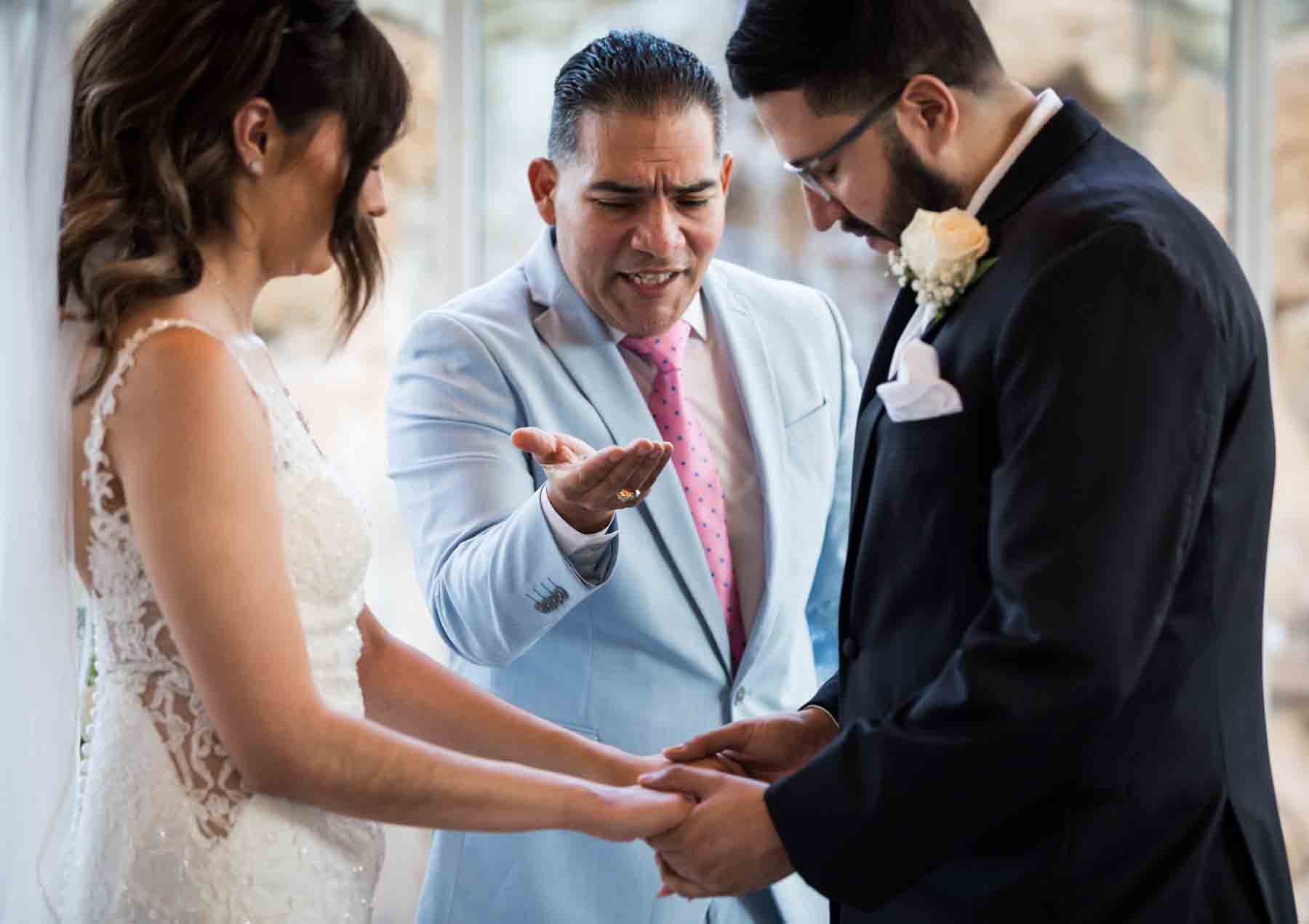 Old San Francisco wedding photos of bride and groom holding hands with officiant holding rings in hand in background