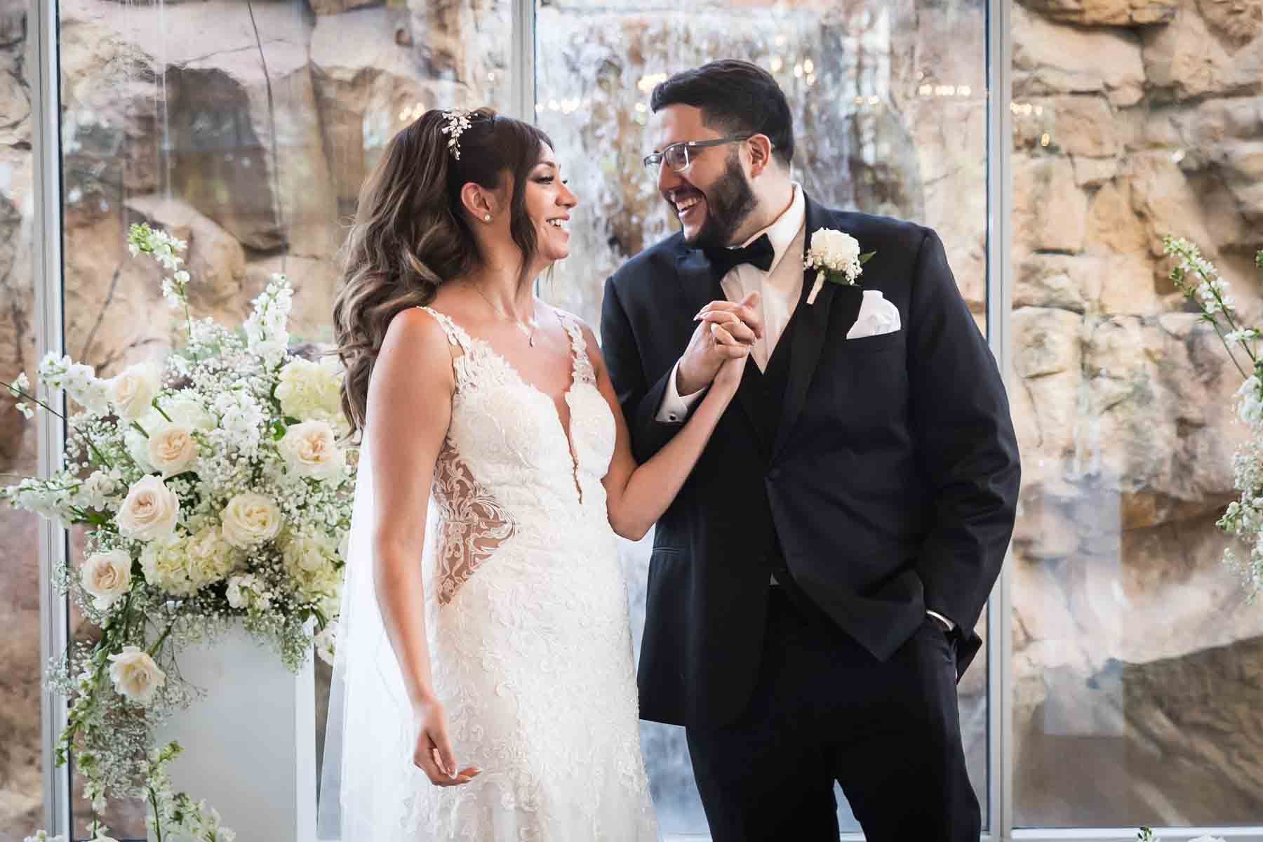 Old San Francisco wedding photos of bride and groom holding hands in front of glass wall and white column holding bouquet of white flowers