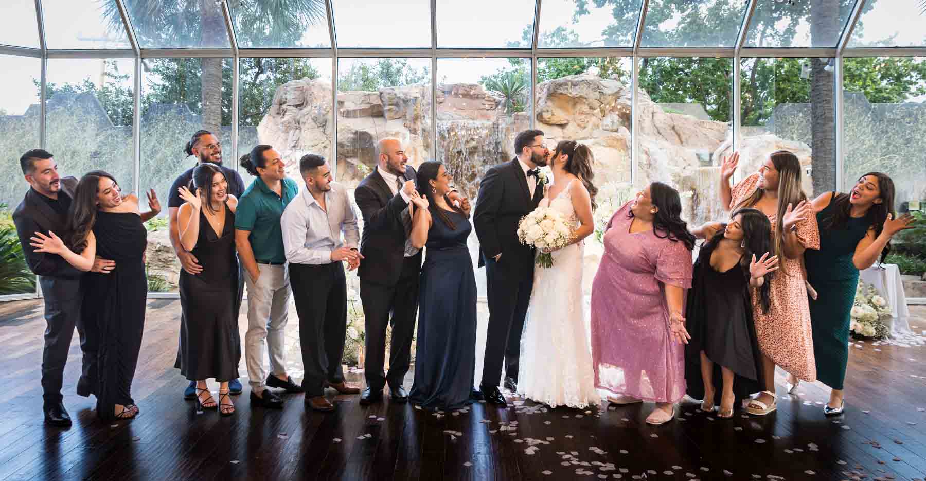 Bride and groom kissing in front of large group of friends in front of glass wall at an Old San Francisco Steakhouse wedding