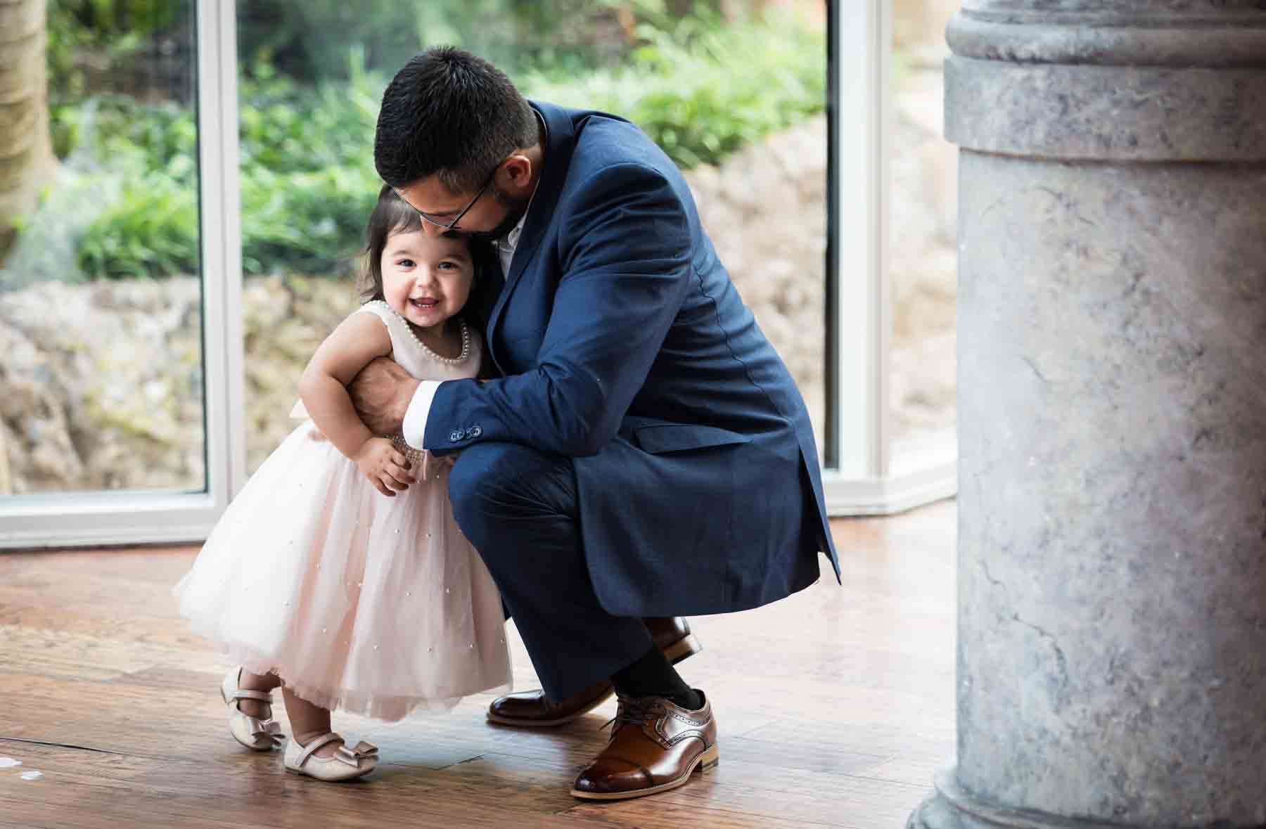 Man bending down to hug smiling little girl wearing pink dress at an Old San Francisco Steakhouse wedding