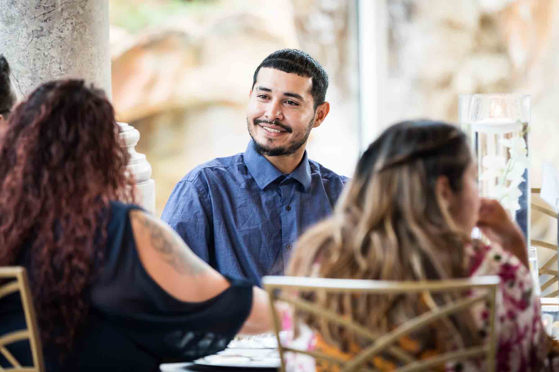 Man with moustache, beard, and nose ring smiling while sitting at table at an Old San Francisco Steakhouse wedding