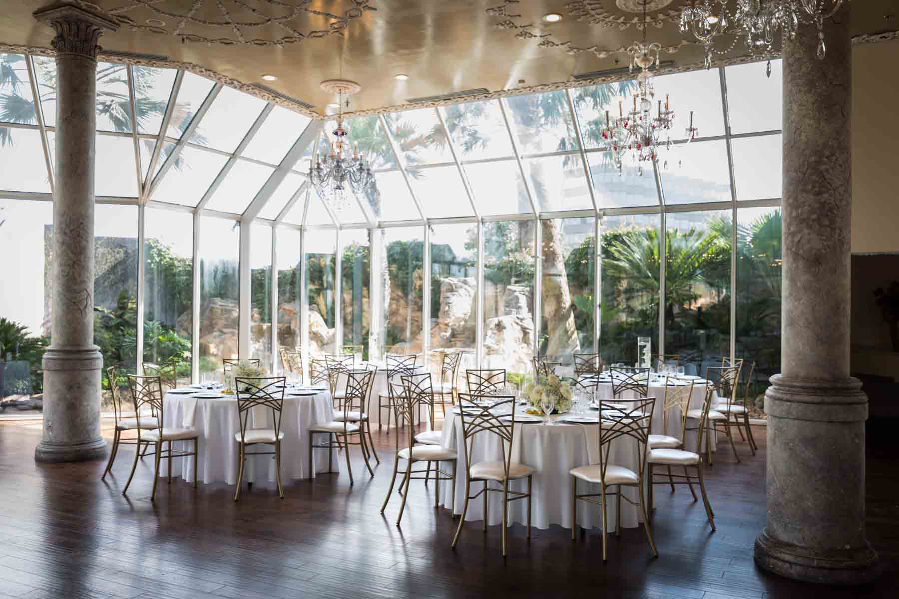 Tables set with white table cloths and low centerpieces in front of glass wall at an Old San Francisco Steakhouse wedding