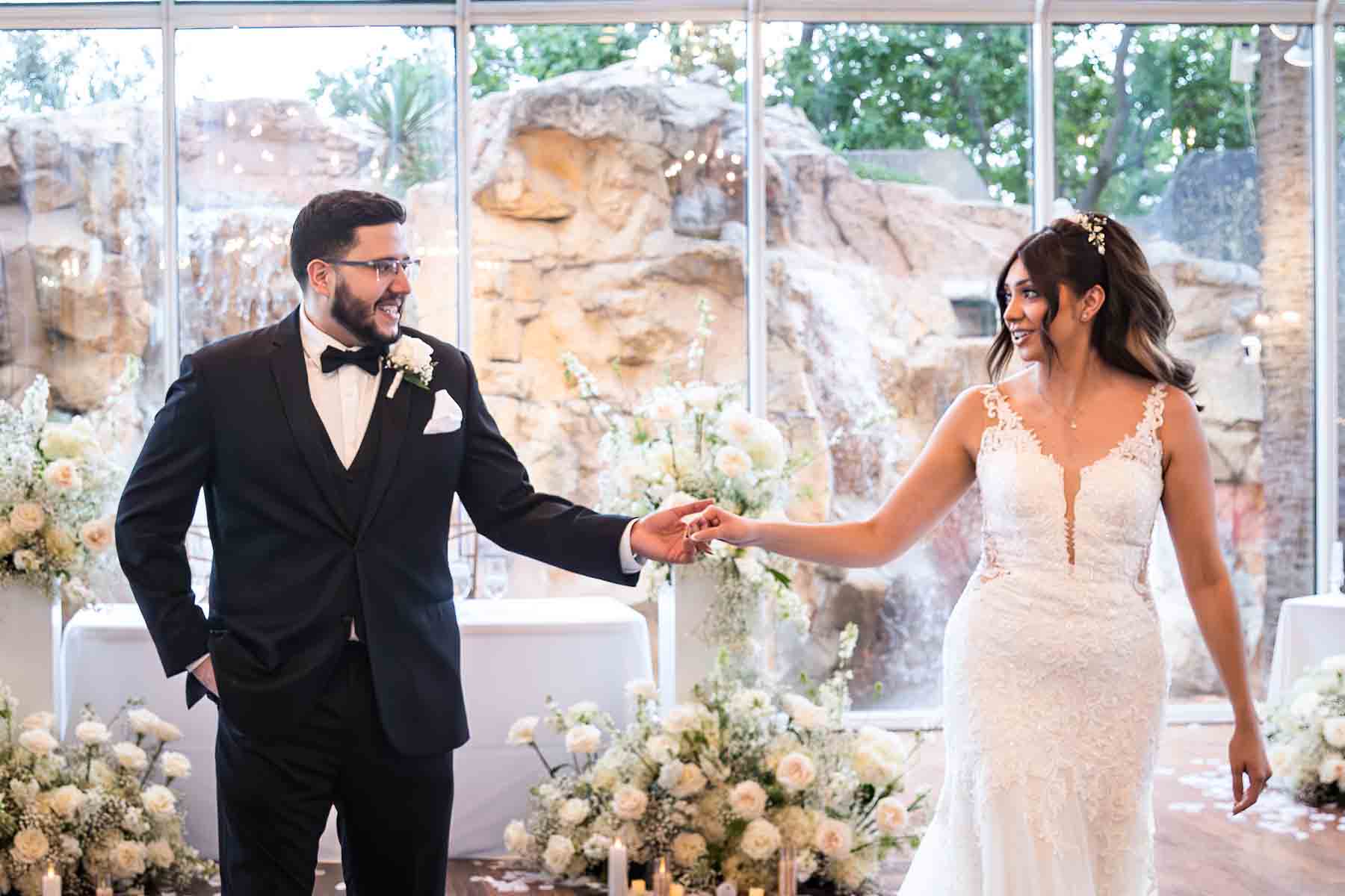 Old San Francisco wedding photos bride and groom holding hands in front of glass wall and white flowers