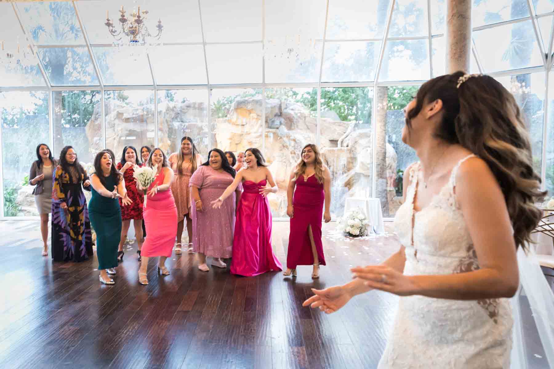 Bride throwing bouquet to group of female guests standing in front of glass wall at an Old San Francisco Steakhouse wedding