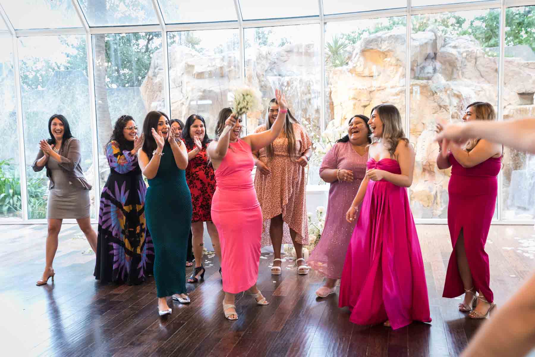 Woman in pink dress holding up bouquet in front of other female guests at an Old San Francisco Steakhouse wedding