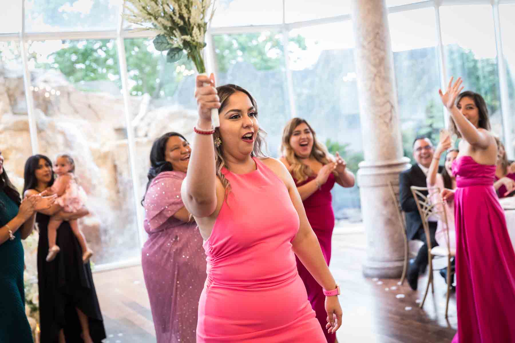 Woman in pink dress holding up bouquet in front of other female guests at an Old San Francisco Steakhouse wedding