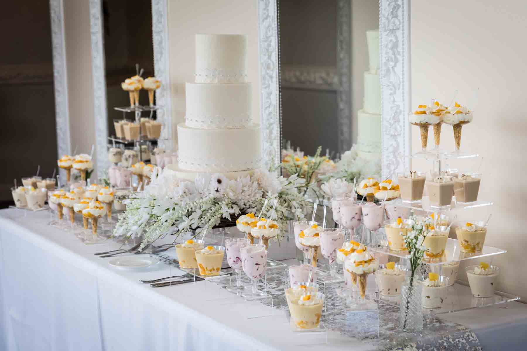 Table filled with desserts in dishes and a wedding cake surrounded by flowers at an Old San Francisco Steakhouse wedding