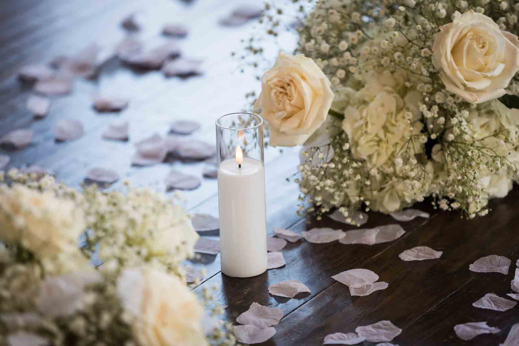 Fake candle on wood floor surrounded by flower petals and bouquets of white roses and babies breath at an Old San Francisco Steakhouse wedding