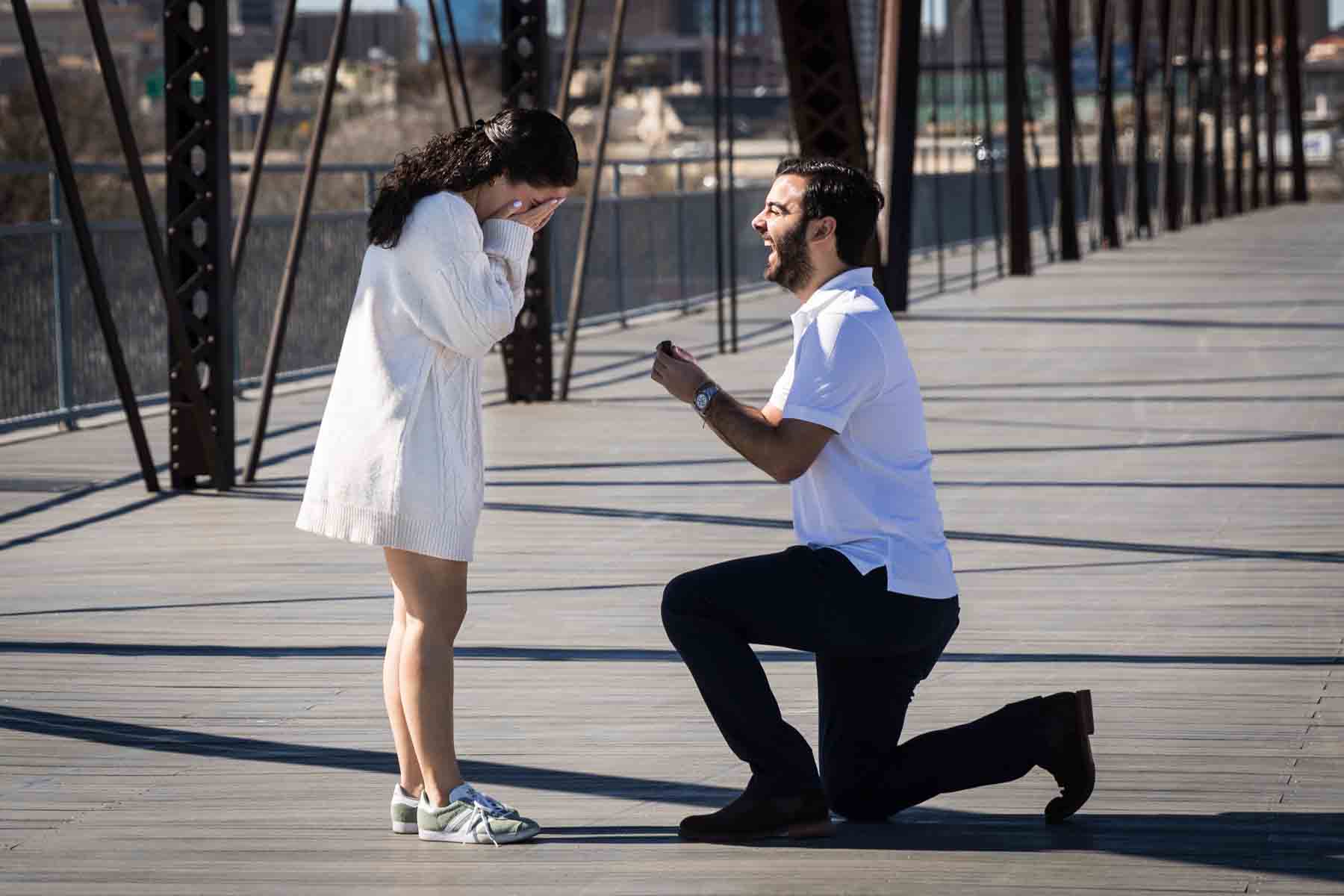 Man on one knee proposing to woman at the Hays Street Bridge