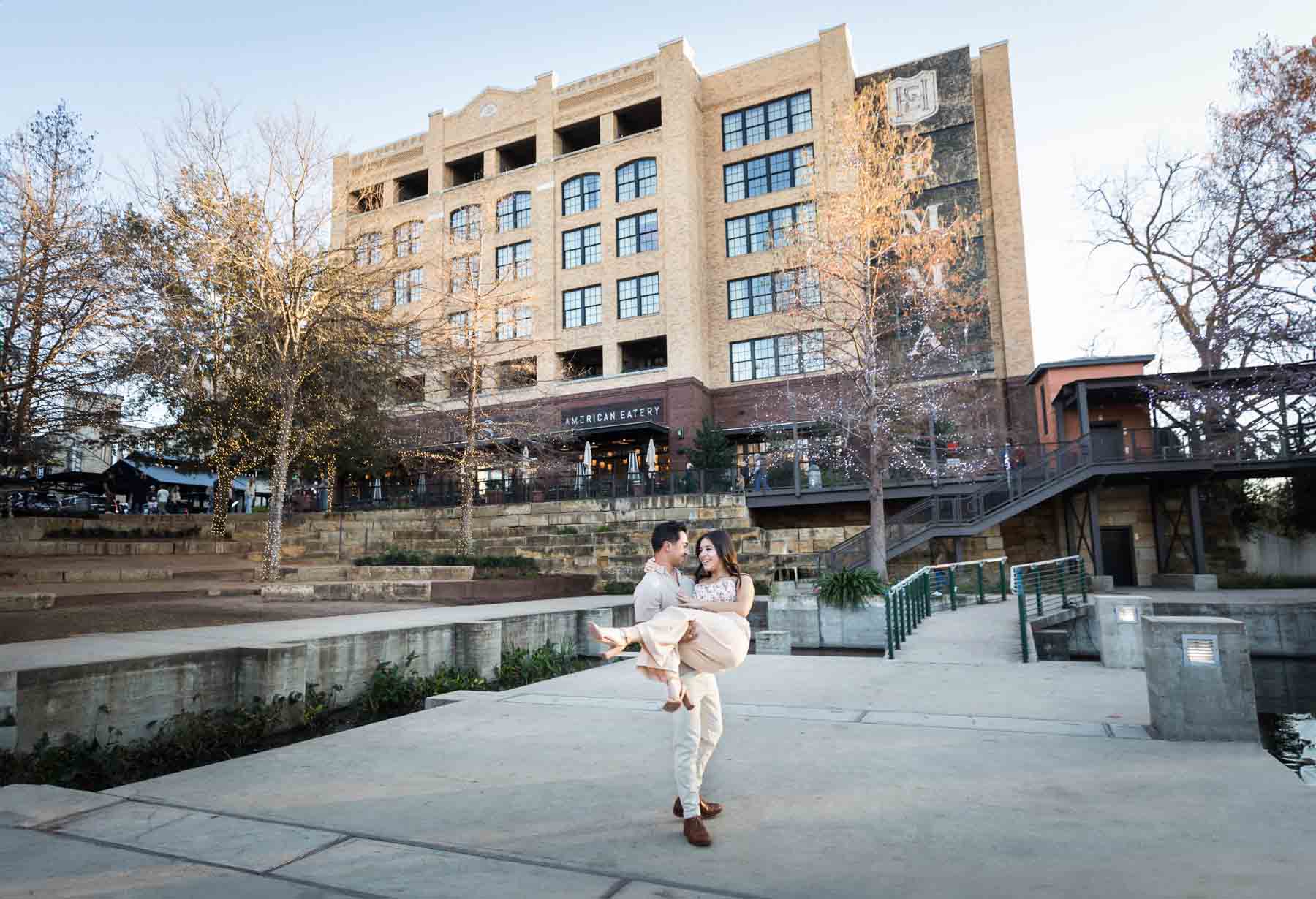 Man holding woman in his arms on platform with Hotel Emma in the background at the Pearl for an article listing the best places to propose in San Antonio