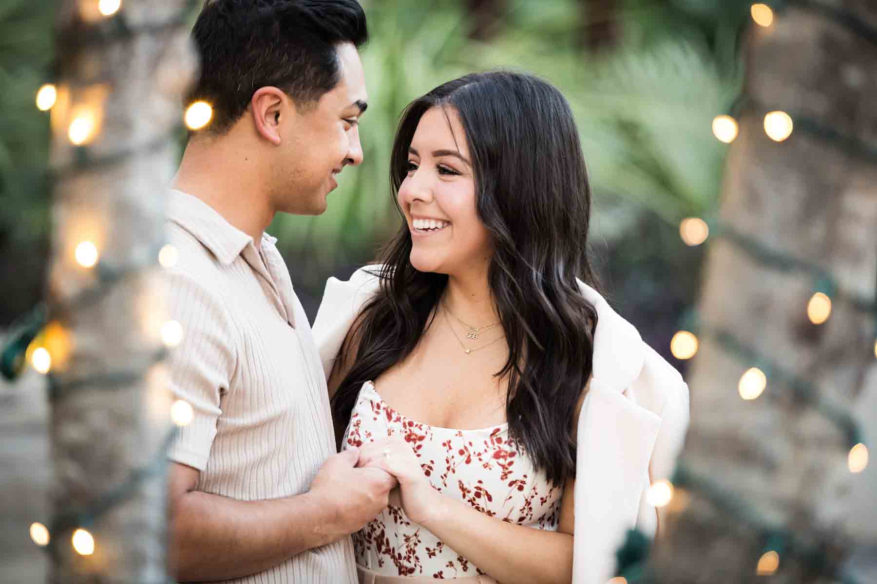 Couple holding hands in front of trees at the Pearl decorated with string lights