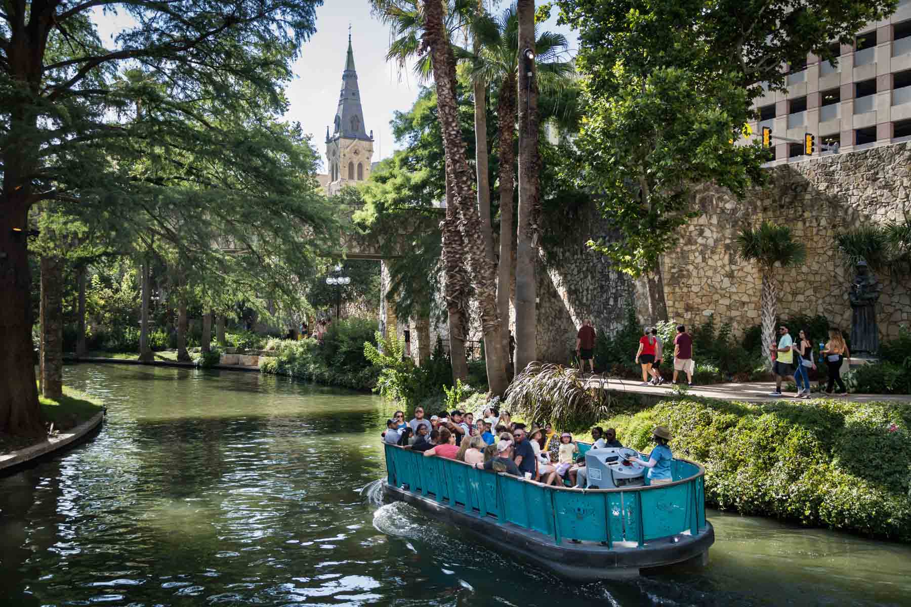 Blue River Walk ferry in river floating past church and palm trees for an article listing the best places to propose in San Antonio