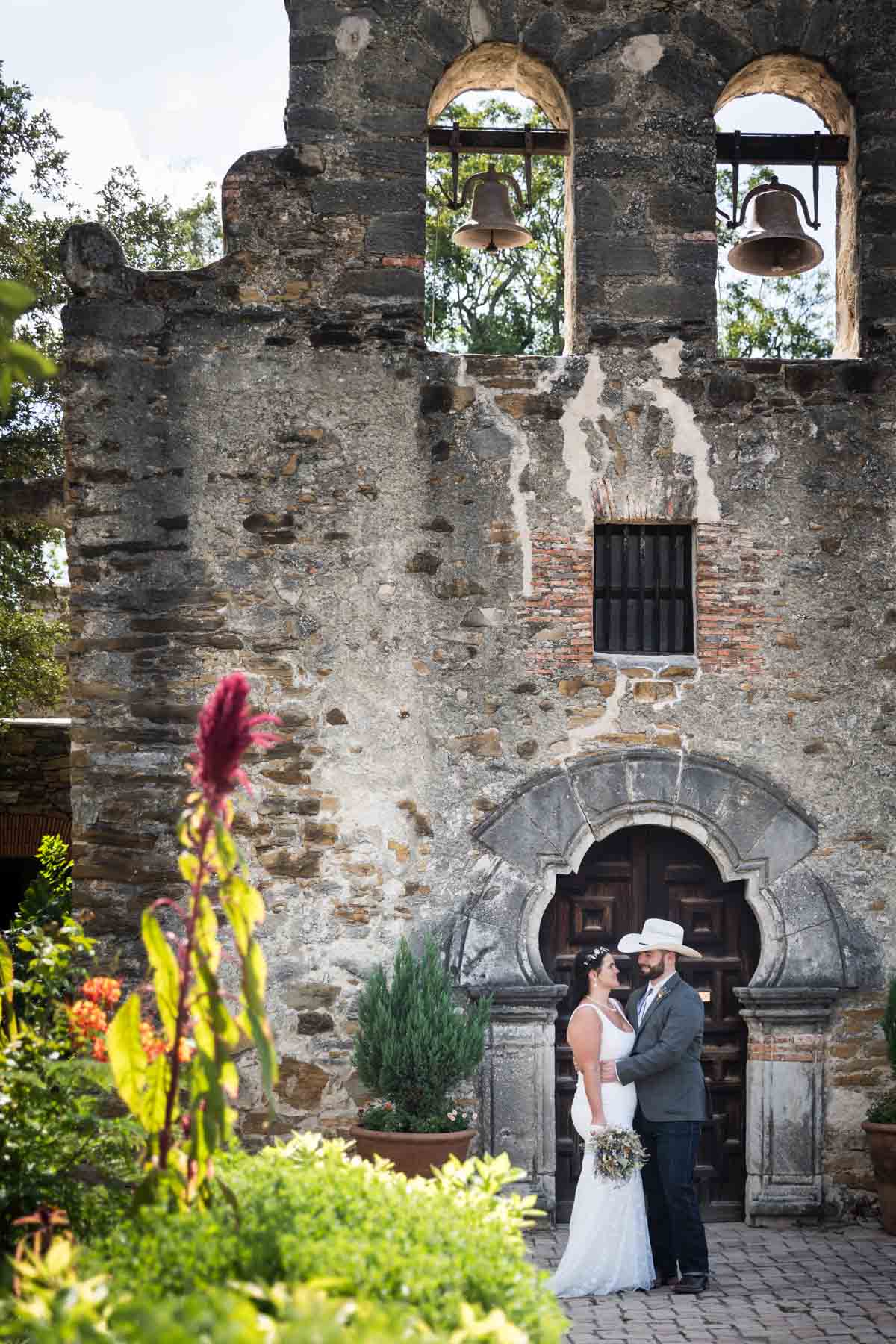 Bride and groom hugging in front of wooden doorway in front of Mission Espada church