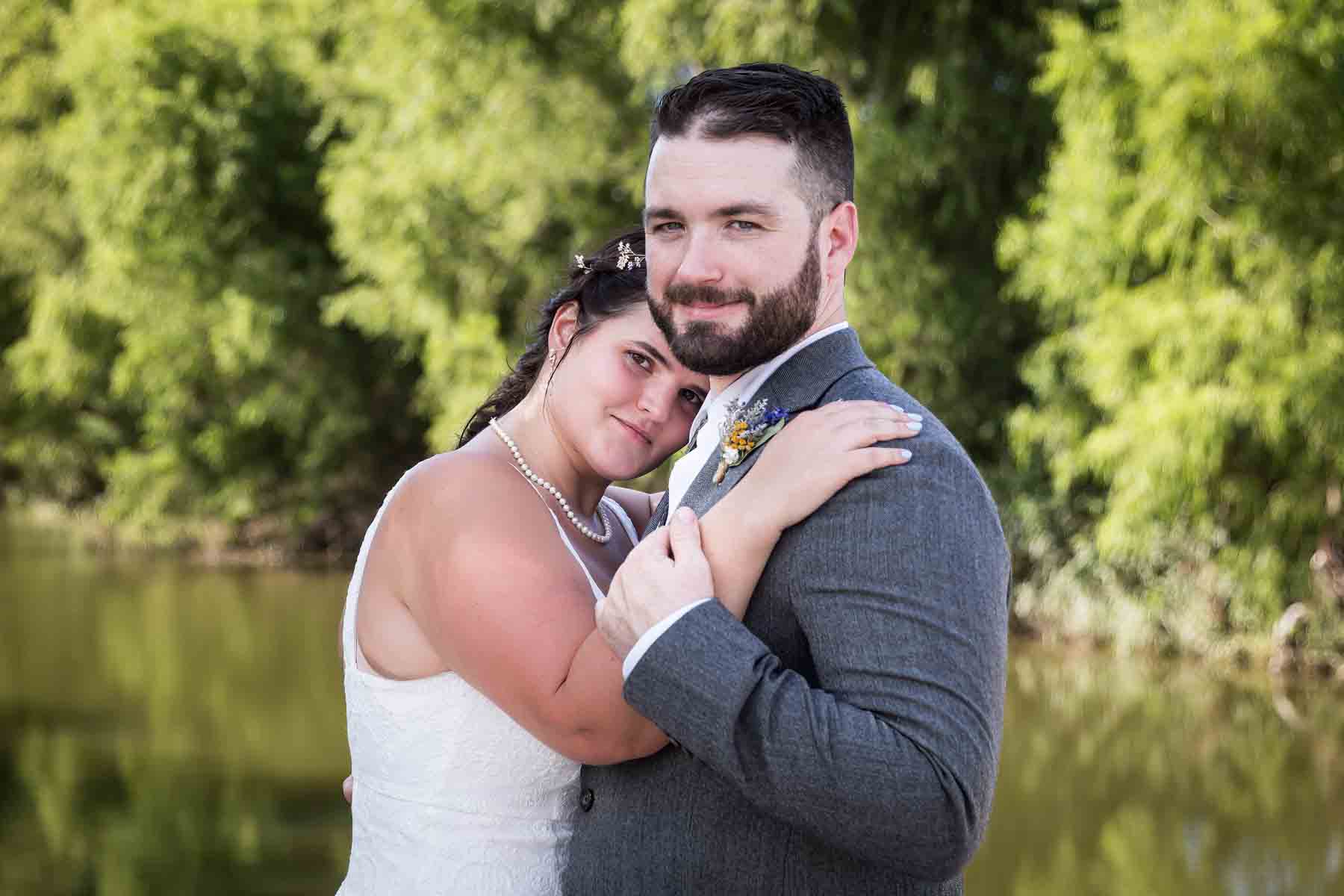 Bride and groom hugging in front of trees and San Antonio River