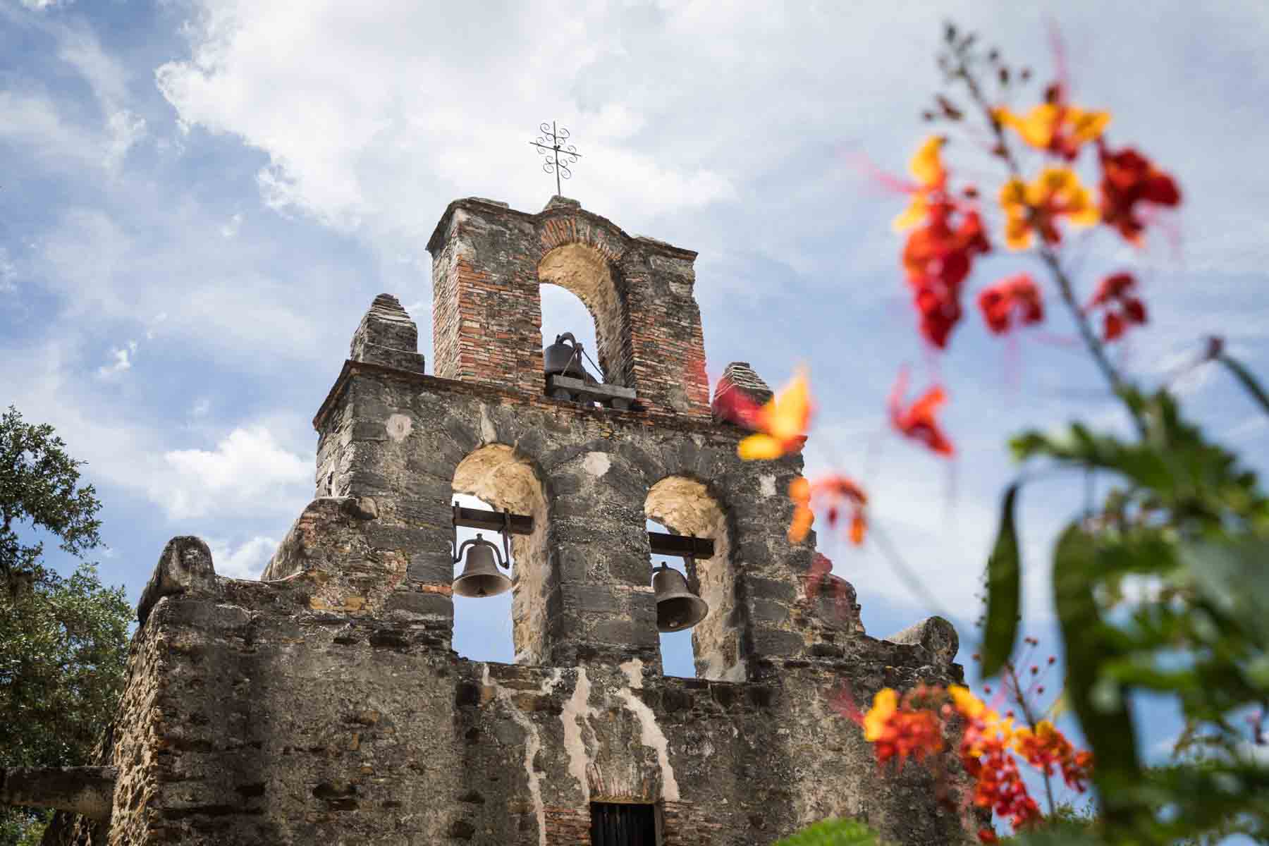 Trefoil bell tower at Mission Espada with orange and red flowers in the foreground for an article listing the best places to propose in San Antonio