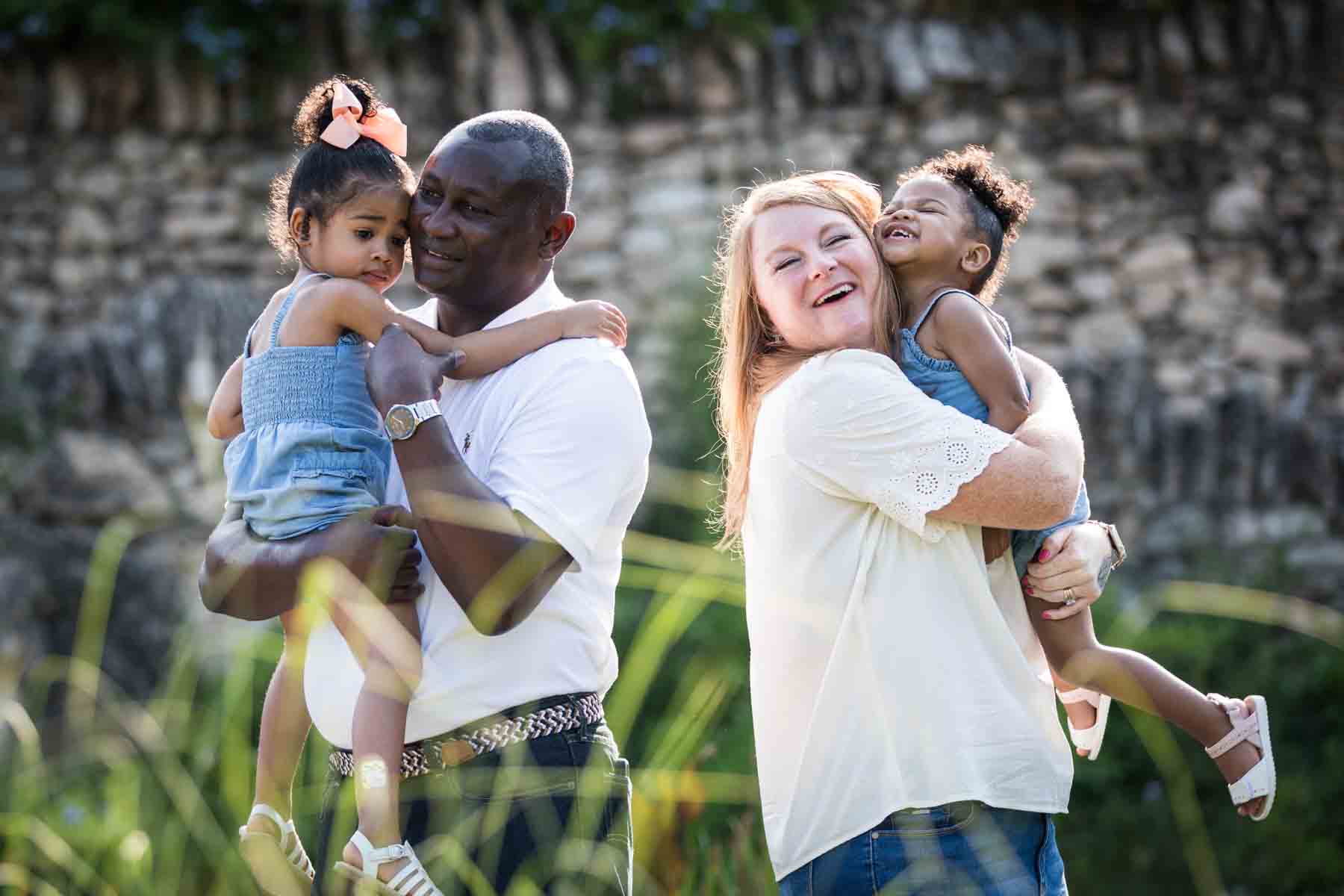 Mixed race couple holding two adorable little girls in front of stone wall at the Japanese Tea Garden for an article on 'How often should I take family photos?'