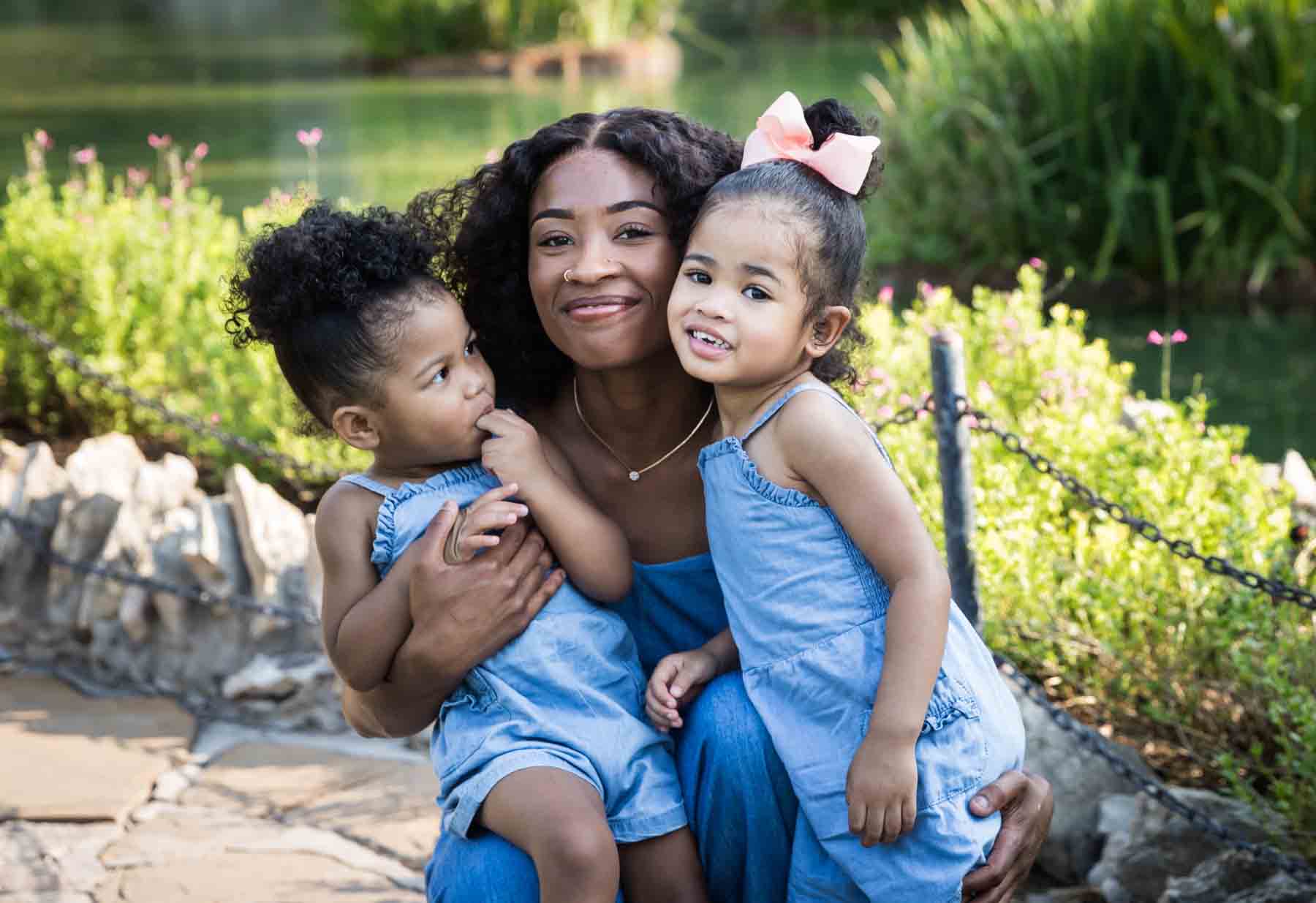 African American mother holding her two adorable daughters in the pathway of the Japanese Tea Garden in front of a pond for an article on 'How often should I take family photos?'