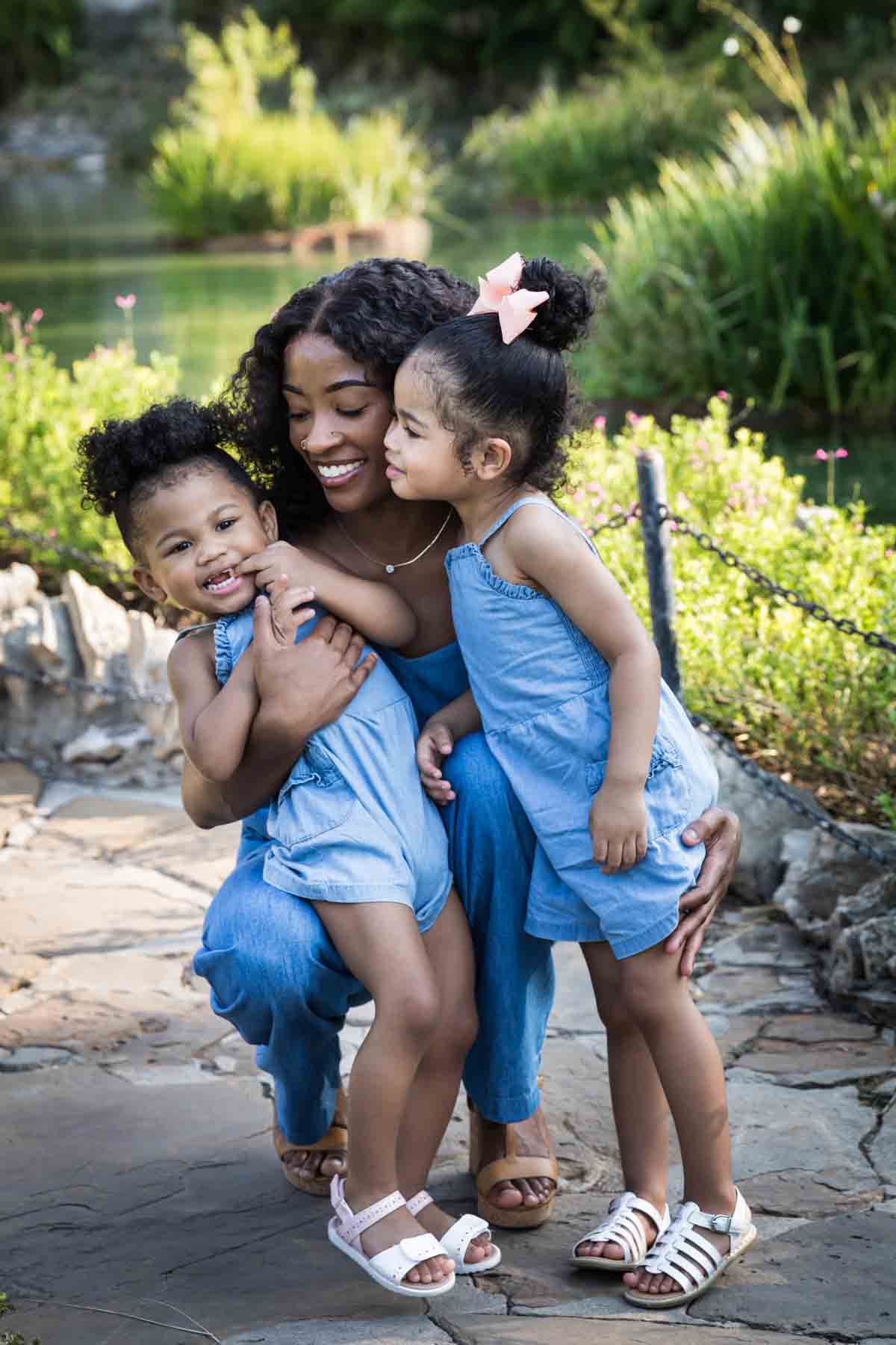 African American mother holding her two adorable daughters in the pathway of the Japanese Tea Garden in front of a pond for an article on 'How often should I take family photos?'