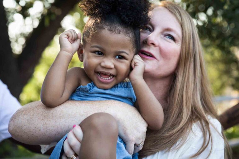 Grandmother holding adorable baby granddaughter with fists raised in front of trees for an article on 'How often should I take family photos?'