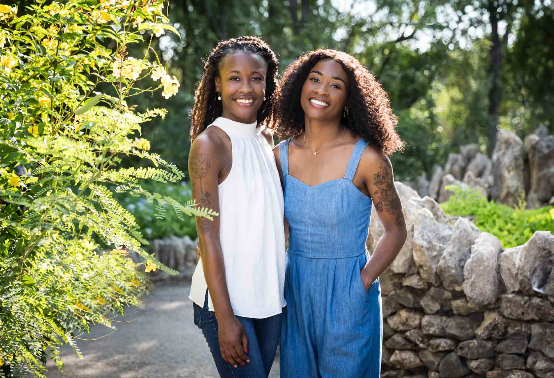 Two African American sisters wearing blue and white standing in the Japanese Tea Garden in front of a bush and stone wall for an article on 'How often should I take family photos?'