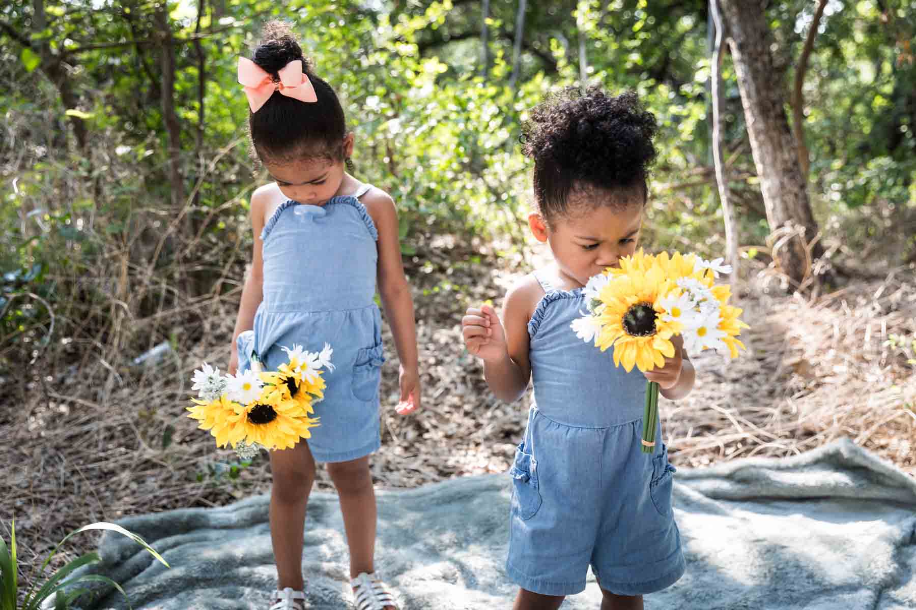 Two little girls looking down at bouquets of daisies and sunflowers in forest of Brackenridge Park