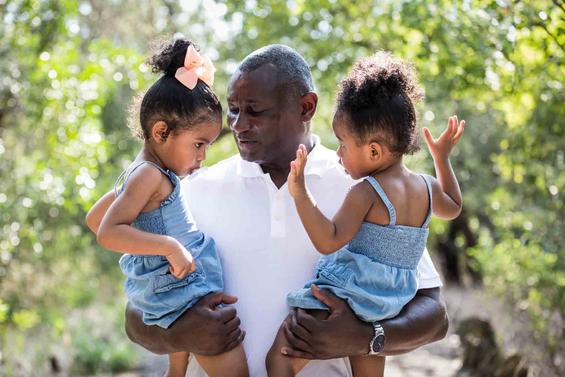 African American grandfather holding two adorable little girls in forest of Brackenridge Park