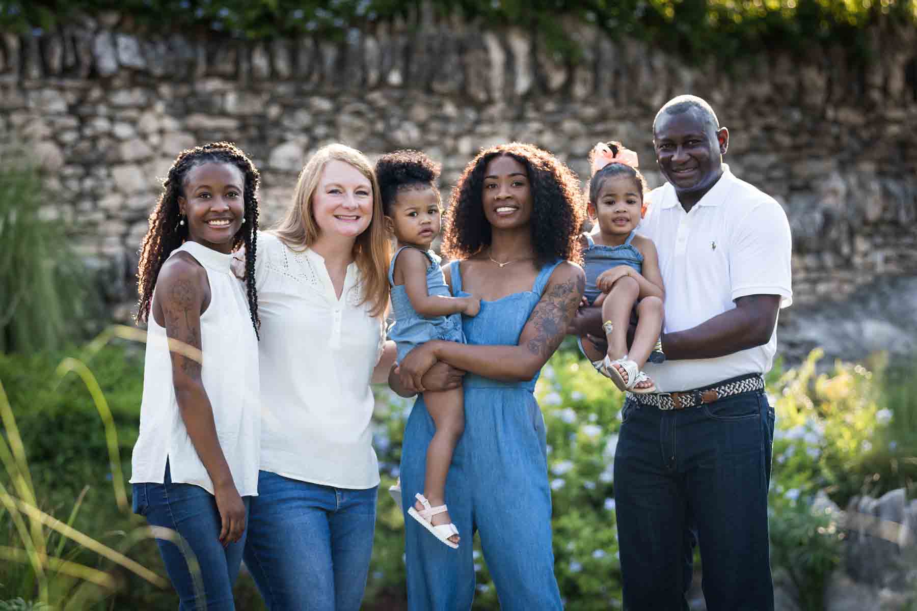 Mixed race family holding two adorable little girls in front of stone wall at the Japanese Tea Garden for an article on 'How often should I take family photos?'