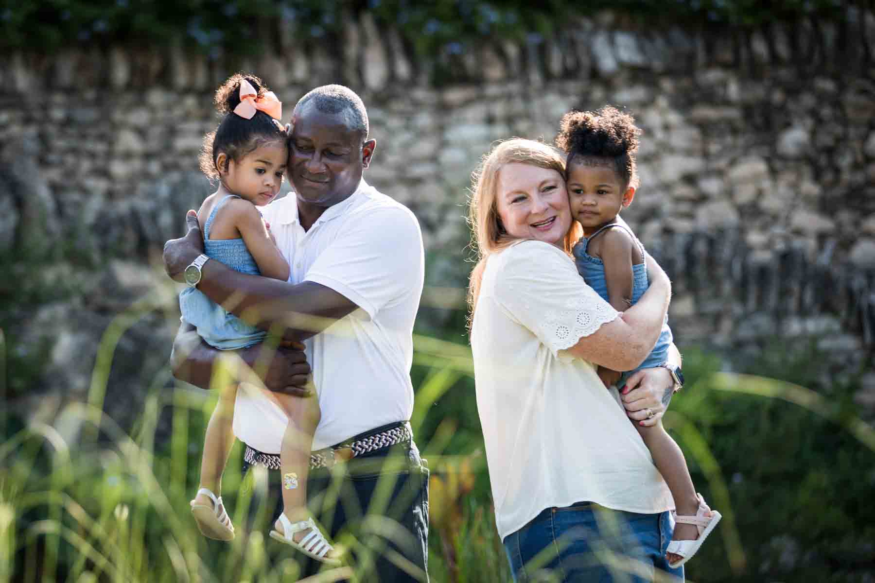 Mixed race couple holding two adorable little girls in front of stone wall at the Japanese Tea Garden for an article on 'How often should I take family photos?'