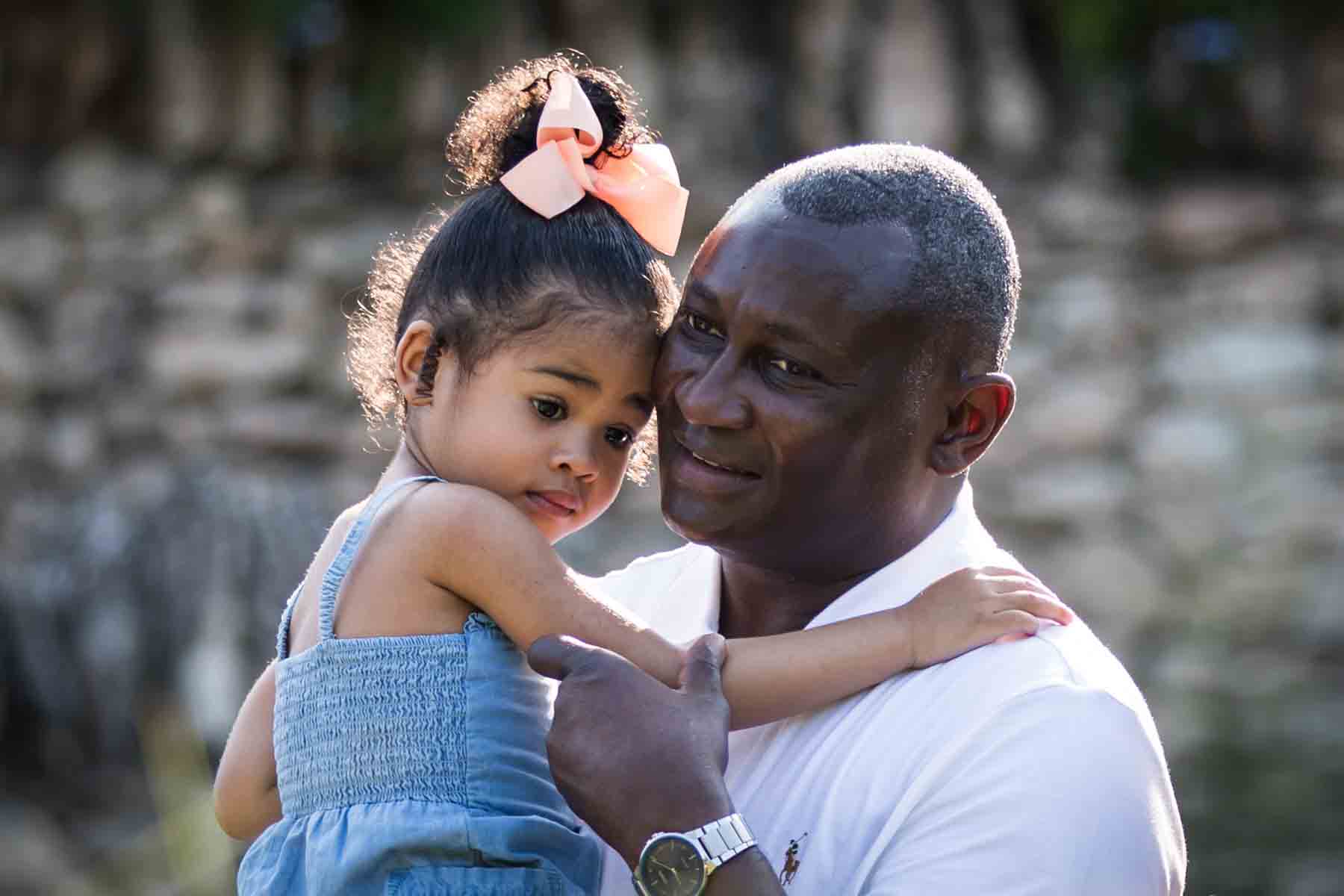 African American man holding adorable little girl in front of stone wall at the Japanese Tea Garden for an article on 'How often should I take family photos?'