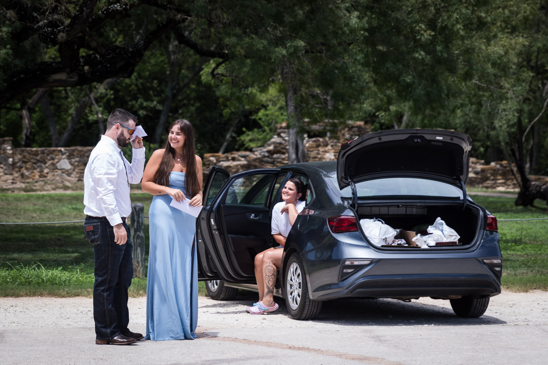 Groom covering eyes speaking to two women in front of car for an article on how to get married at Mission Espada