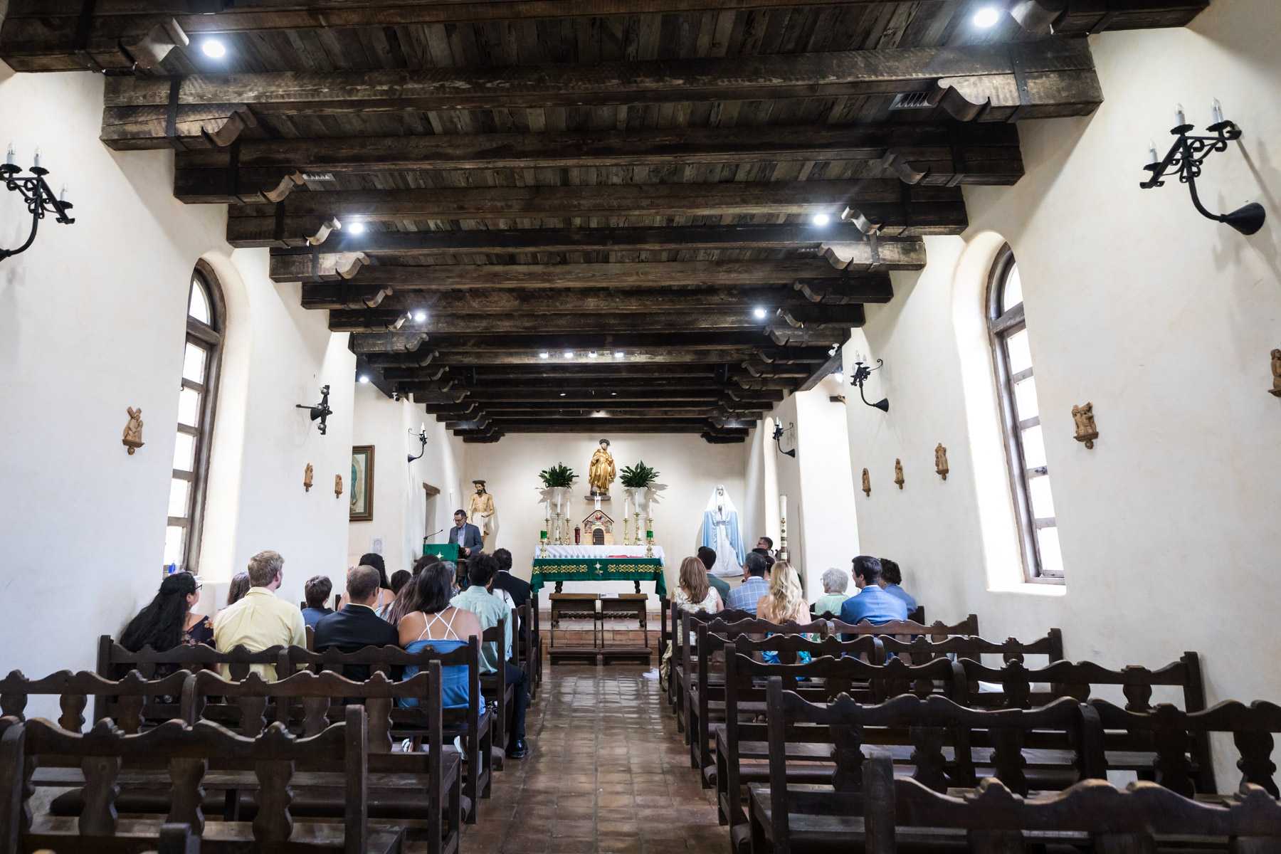 Wide shot of guest speaking during ceremony inside Mission Espada church for an article on how to get married at Mission Espada