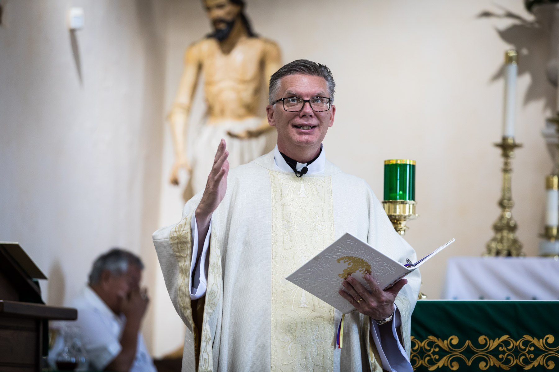 Priest with hand held up looking up at ceiling during ceremony for an article on how to get married at Mission Espada