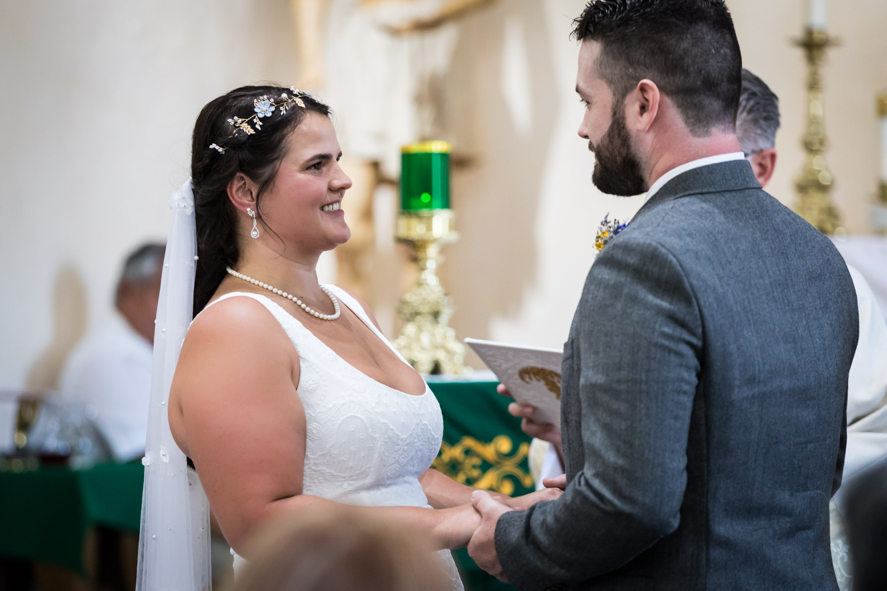 Bride wearing sleeveless white dress and veil holding hands with groom during ceremony for an article on how to get married at Mission Espada