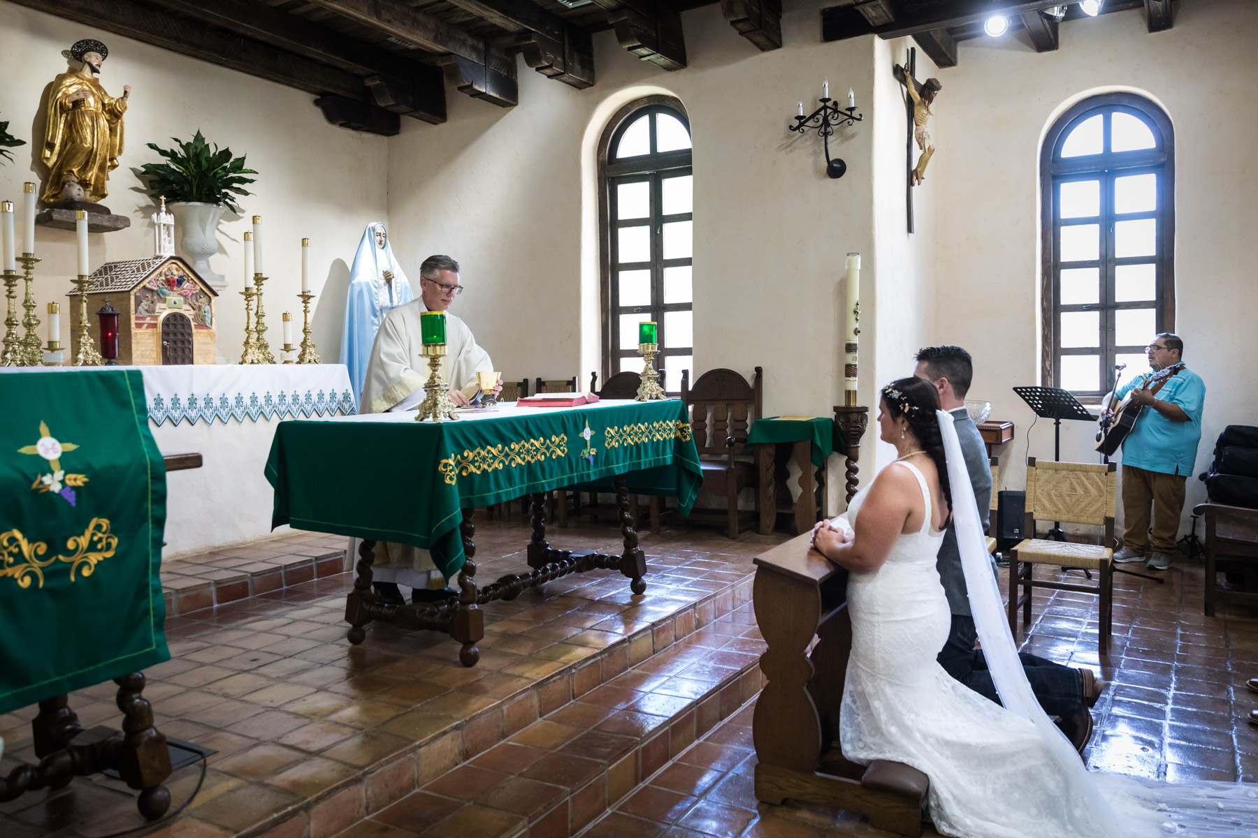 Bride and groom kneeling in front of altar during mass for an article on how to get married at Mission Espada