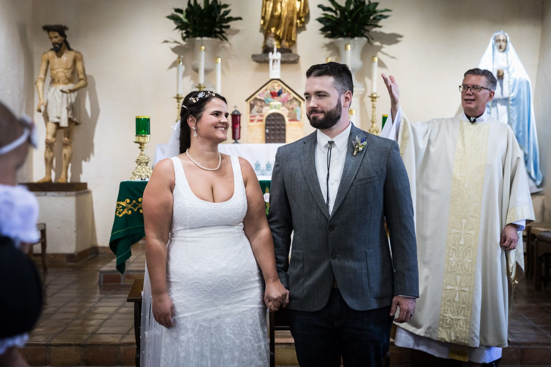 Bride and groom looking at each other in front of altar and priest for an article on how to get married at Mission Espada