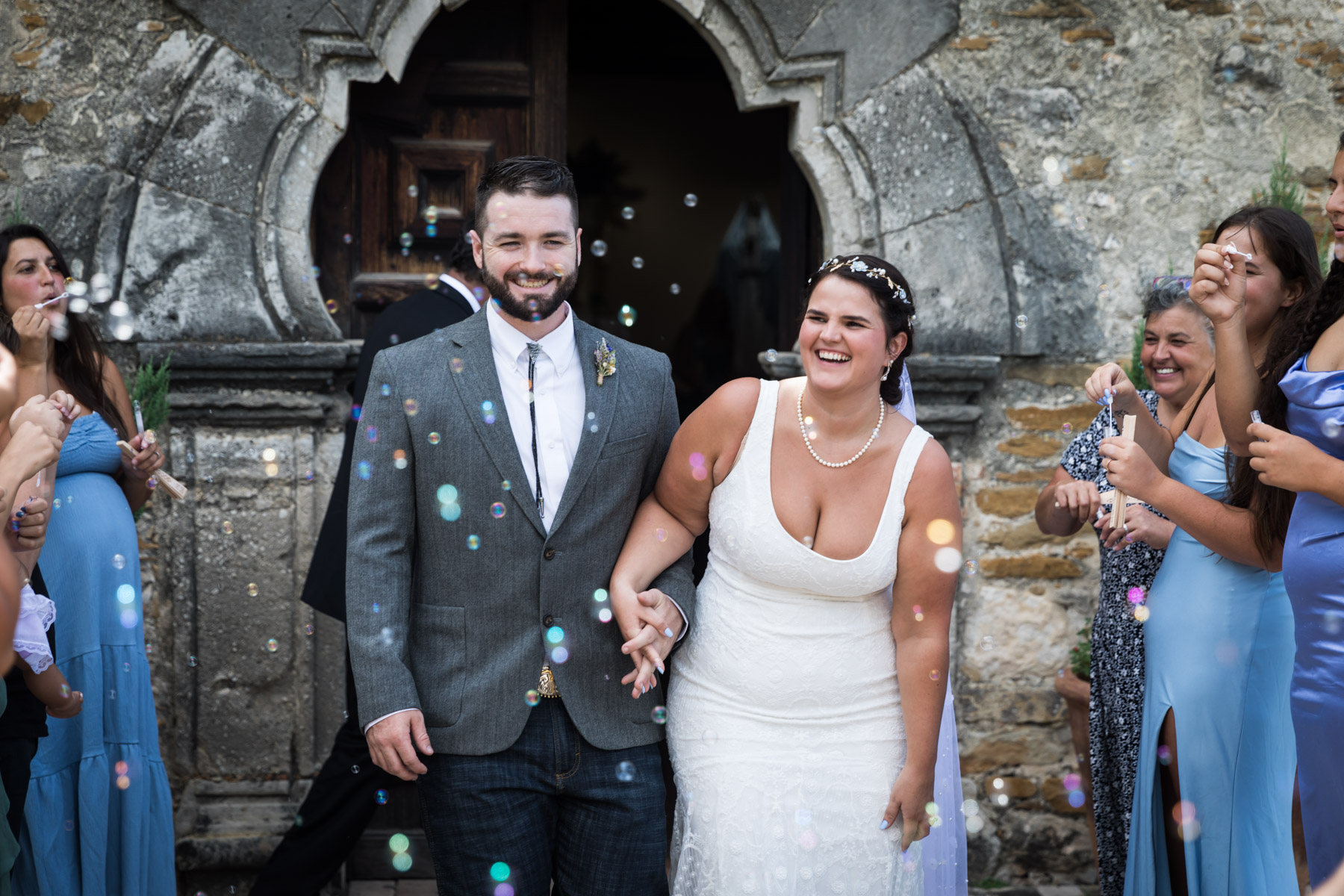 Bride and groom holding hands with bubbles floating around them for an article on how to get married at Mission Espada